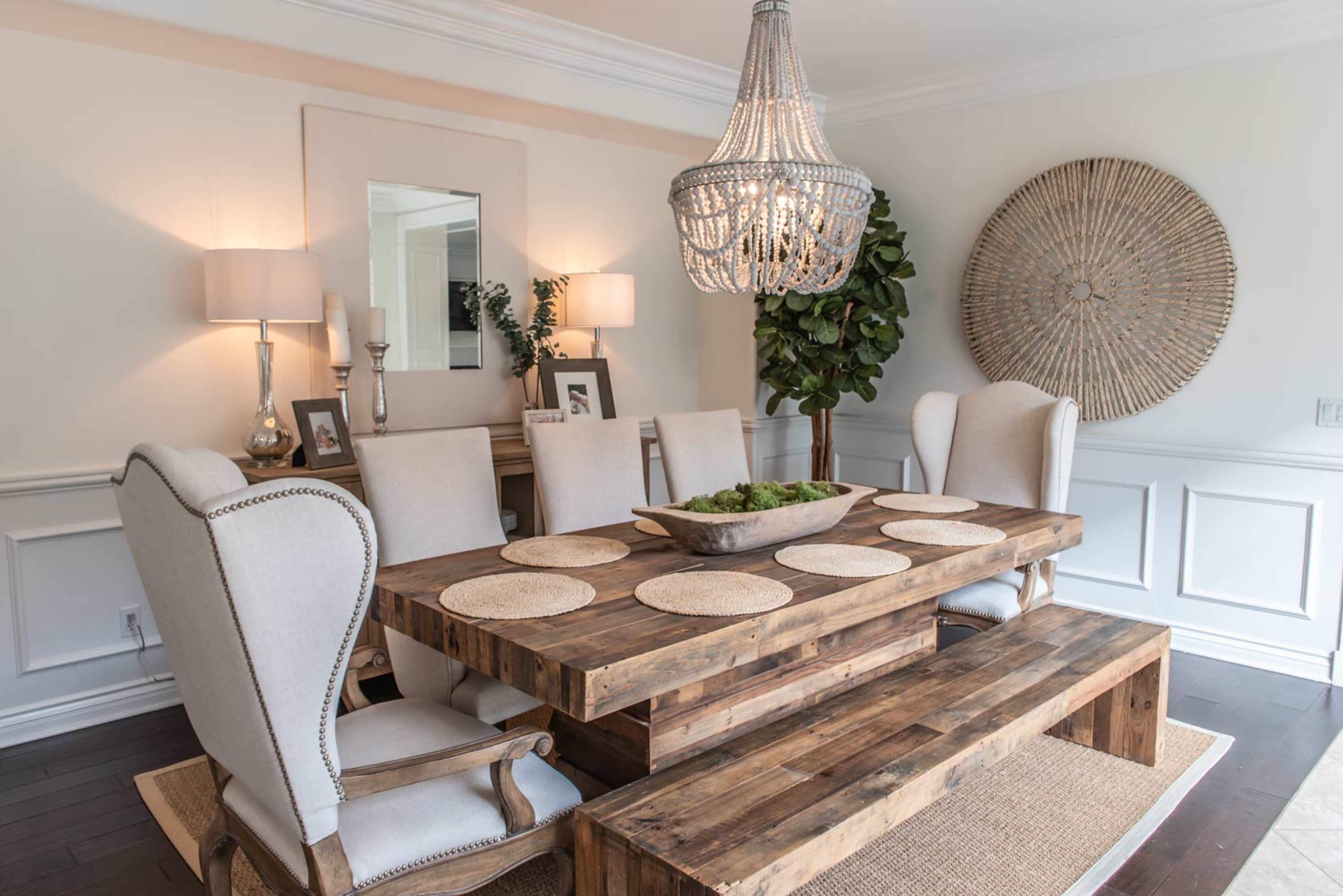 A wooden dining table surrounded by upholstered chairs is set with placemats, and a chandelier hangs above, illuminating the room.