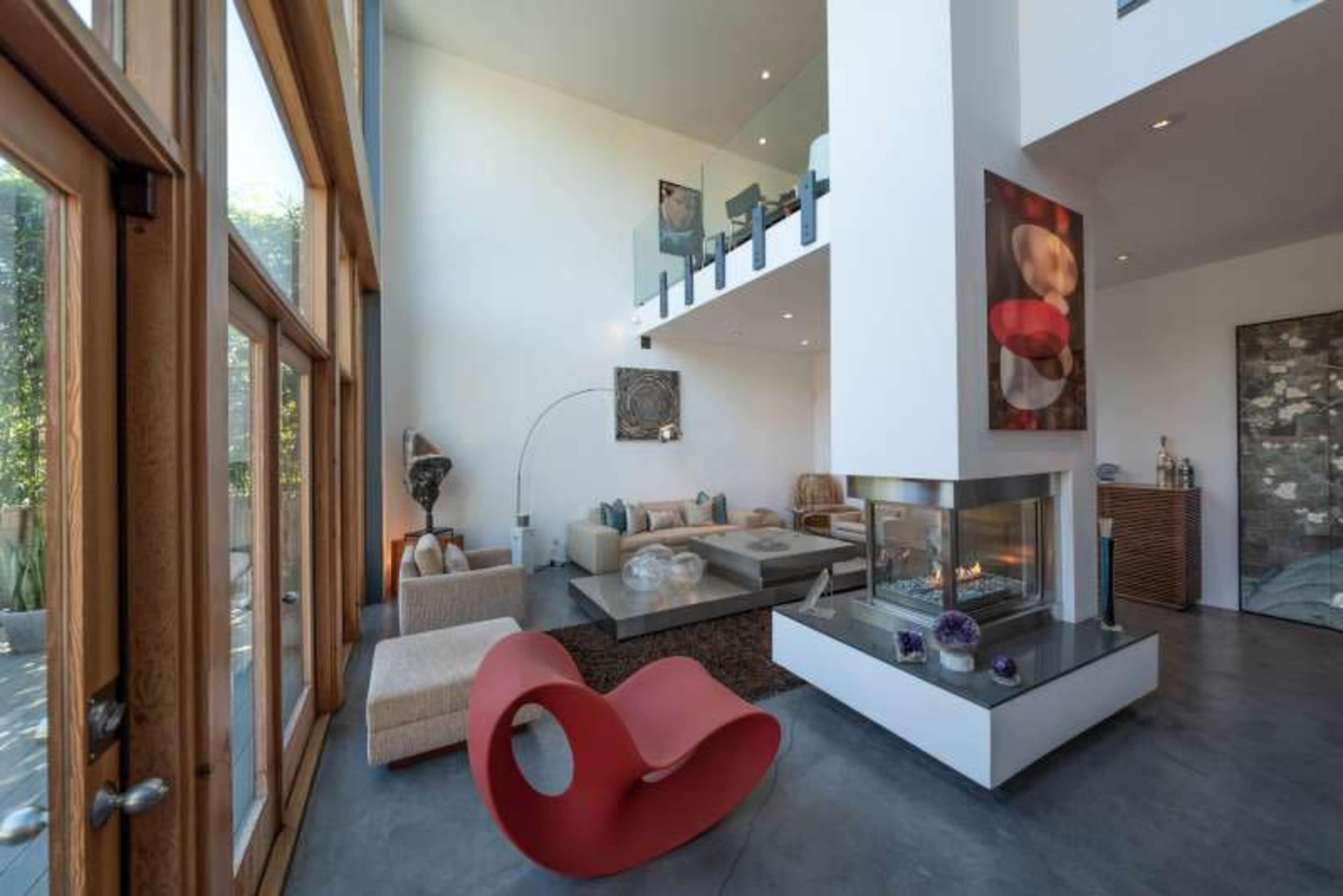 A modern living room with high ceilings, large windows, a contemporary fireplace, and minimalist furniture.