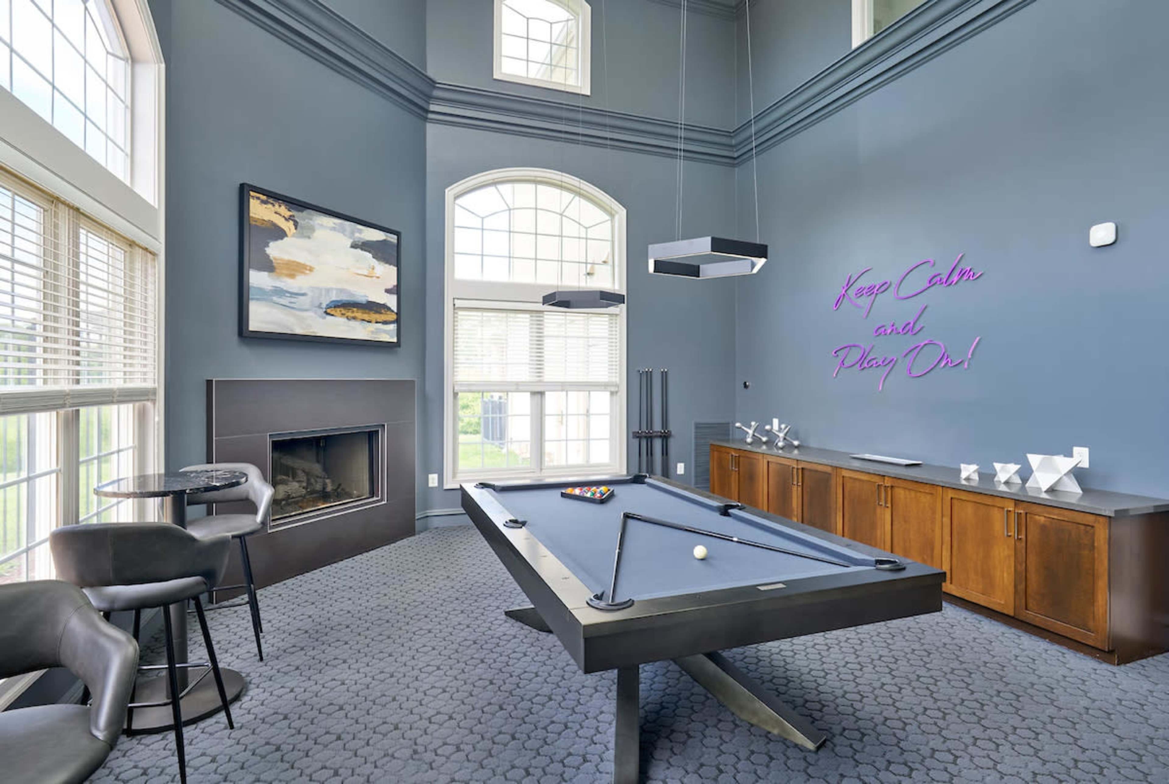 A modern game room features a pool table, a fireplace, and large windows that allow natural light to fill the space.