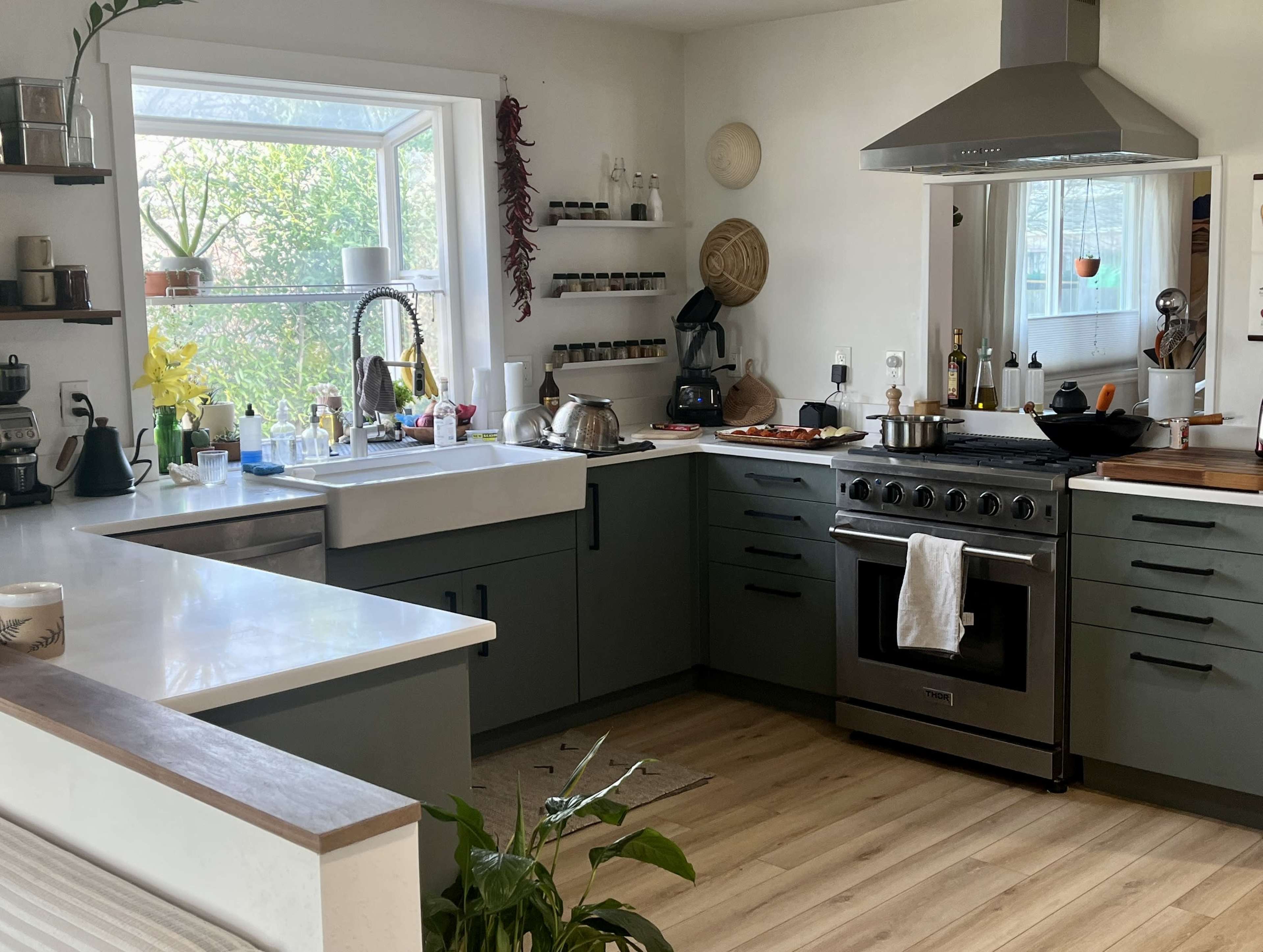 A modern kitchen features a spacious island with a sink, a range hood above a stove, and large windows providing natural light.
