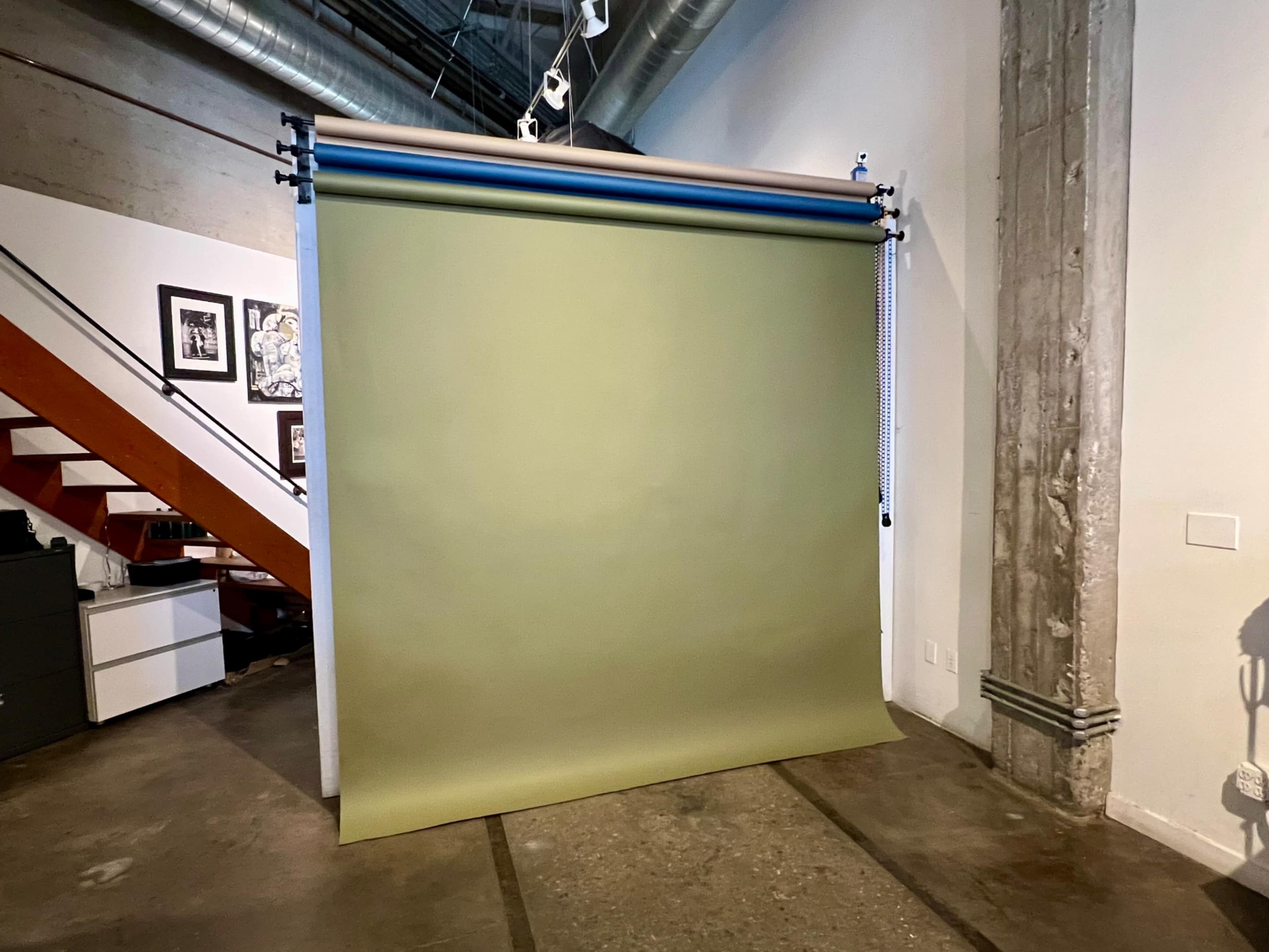 A green backdrop is suspended in an industrial-style space featuring exposed concrete and wooden elements.