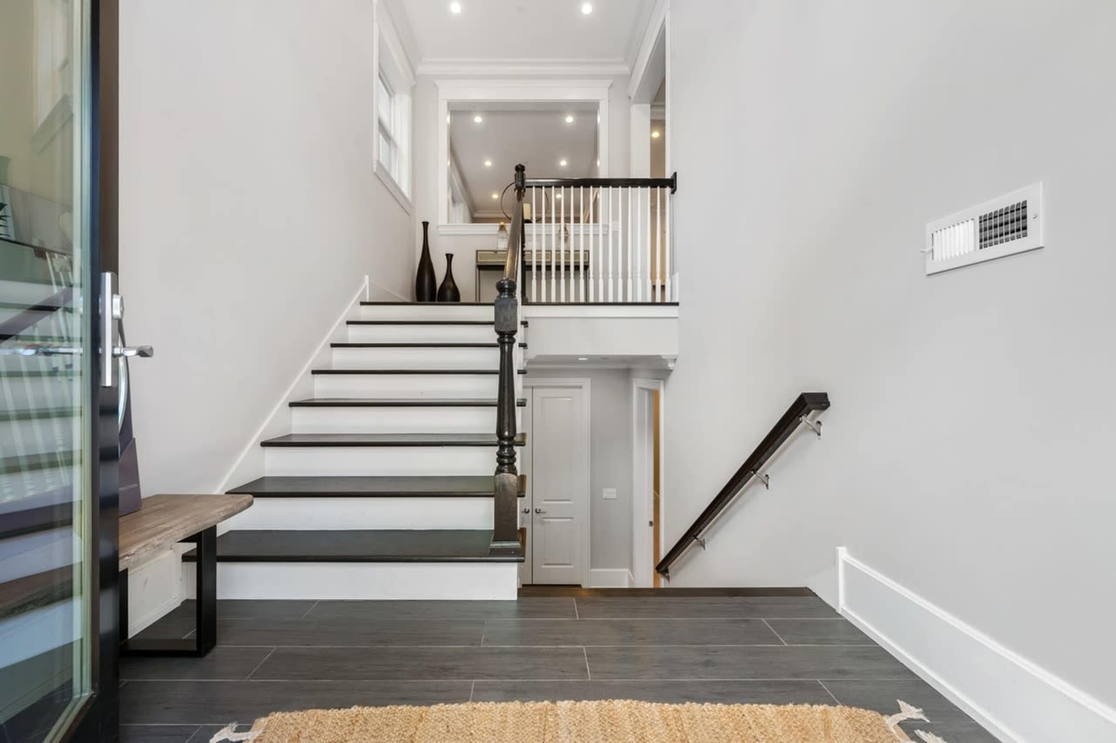 A modern entryway with a staircase leading to a second floor, featuring a mix of dark flooring and light-colored walls.