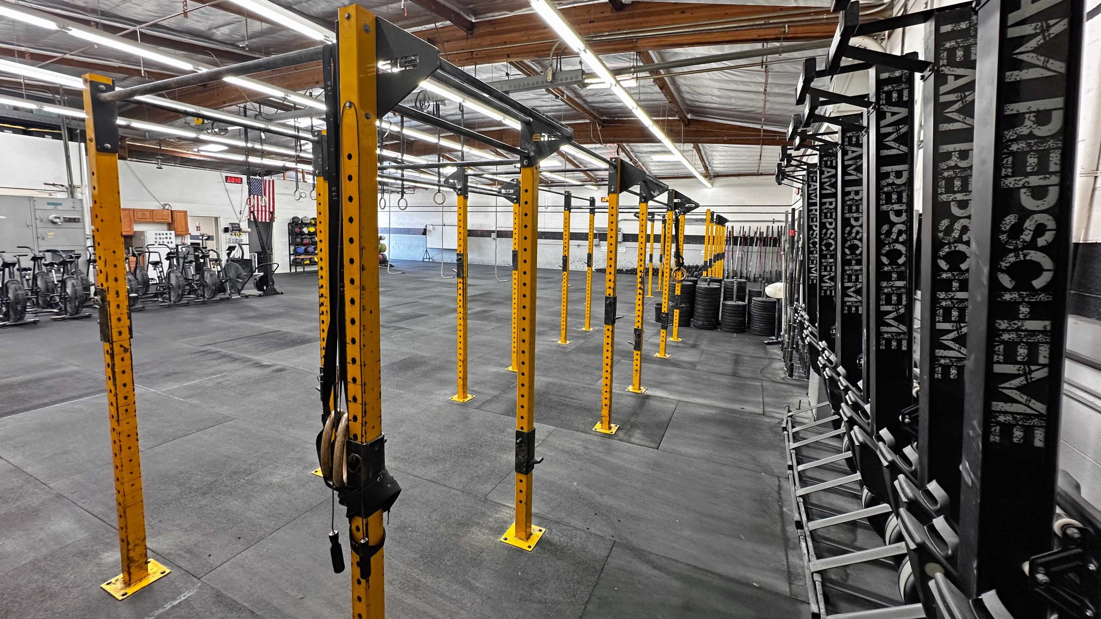 The image shows a spacious gym with numerous yellow workout stations arranged in rows and various exercise equipment in the background.