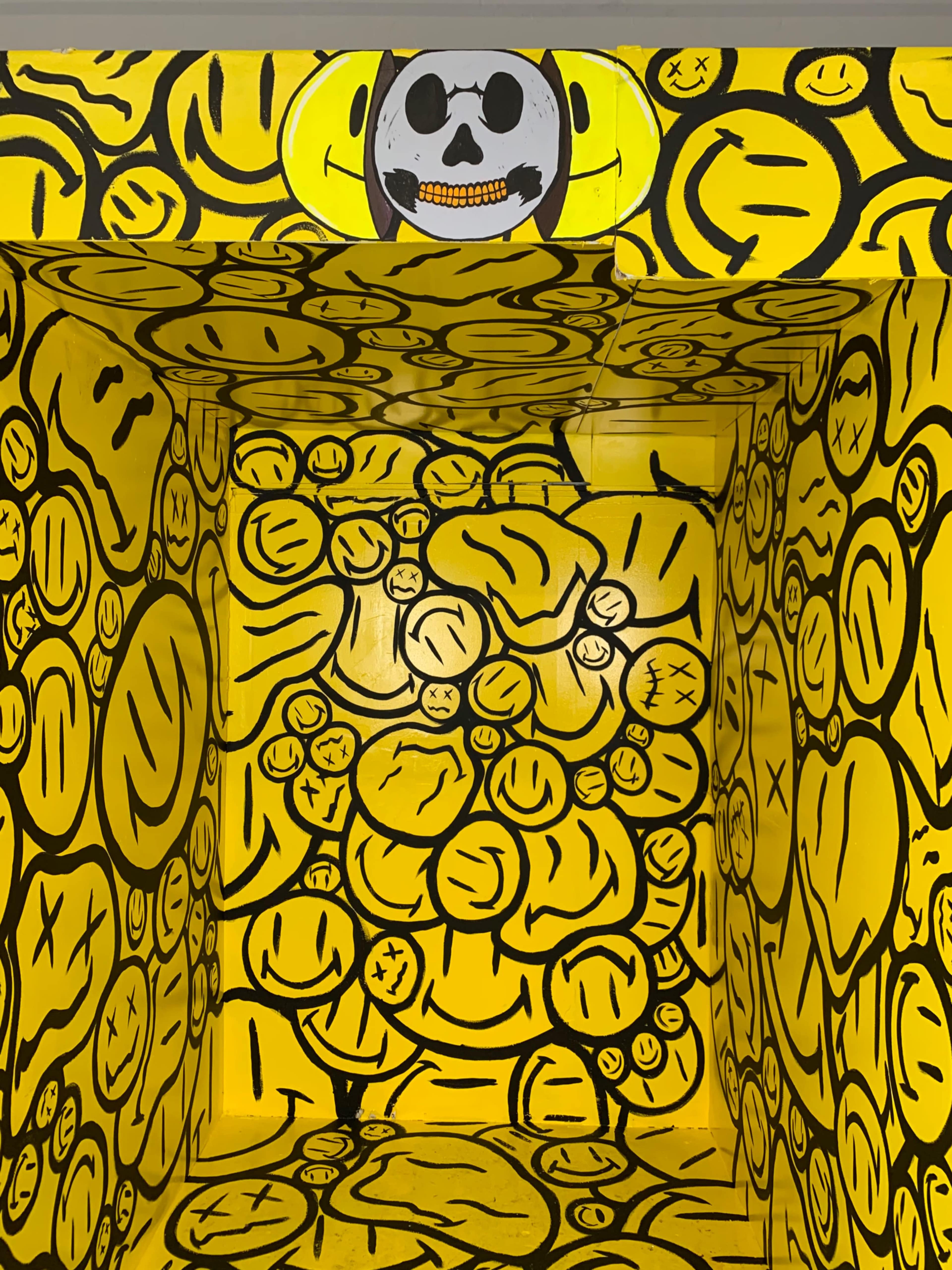 A vividly painted room filled with yellow walls covered in cartoonish smiley faces and a skull design on the ceiling.