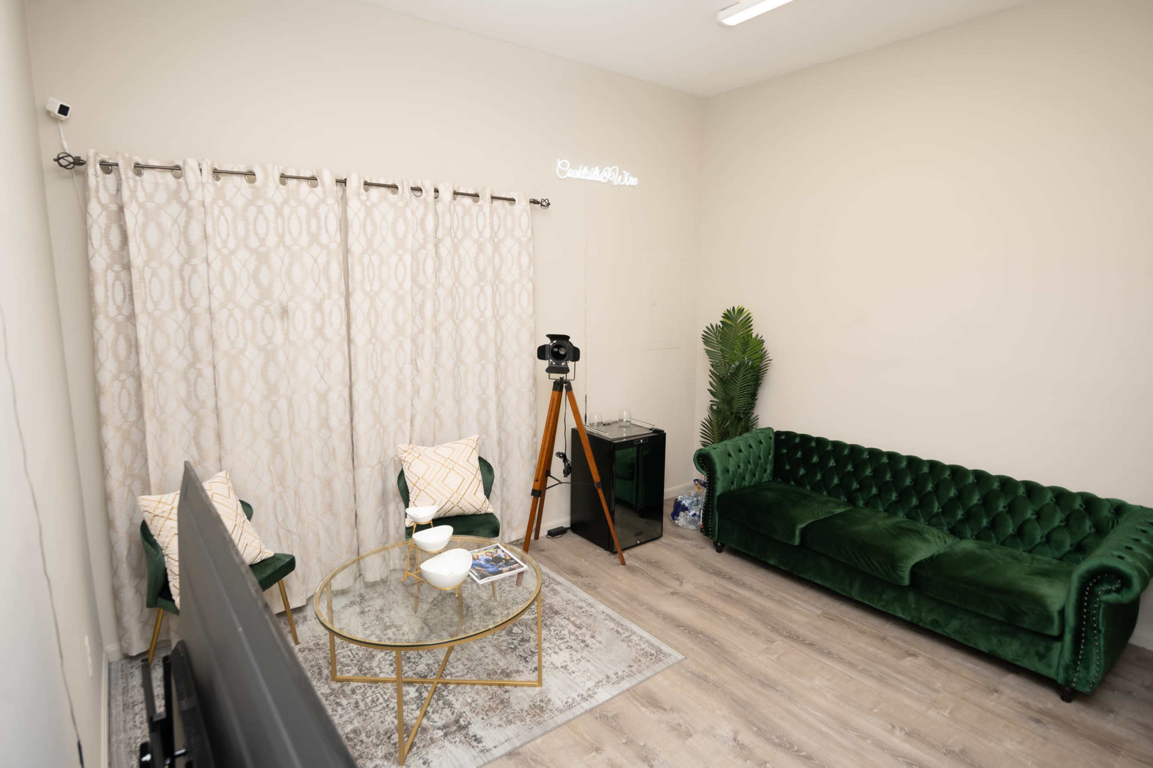 The image shows a cozy room with a green velvet sofa, a glass coffee table, a decorative curtain, and a vintage camera on a tripod.