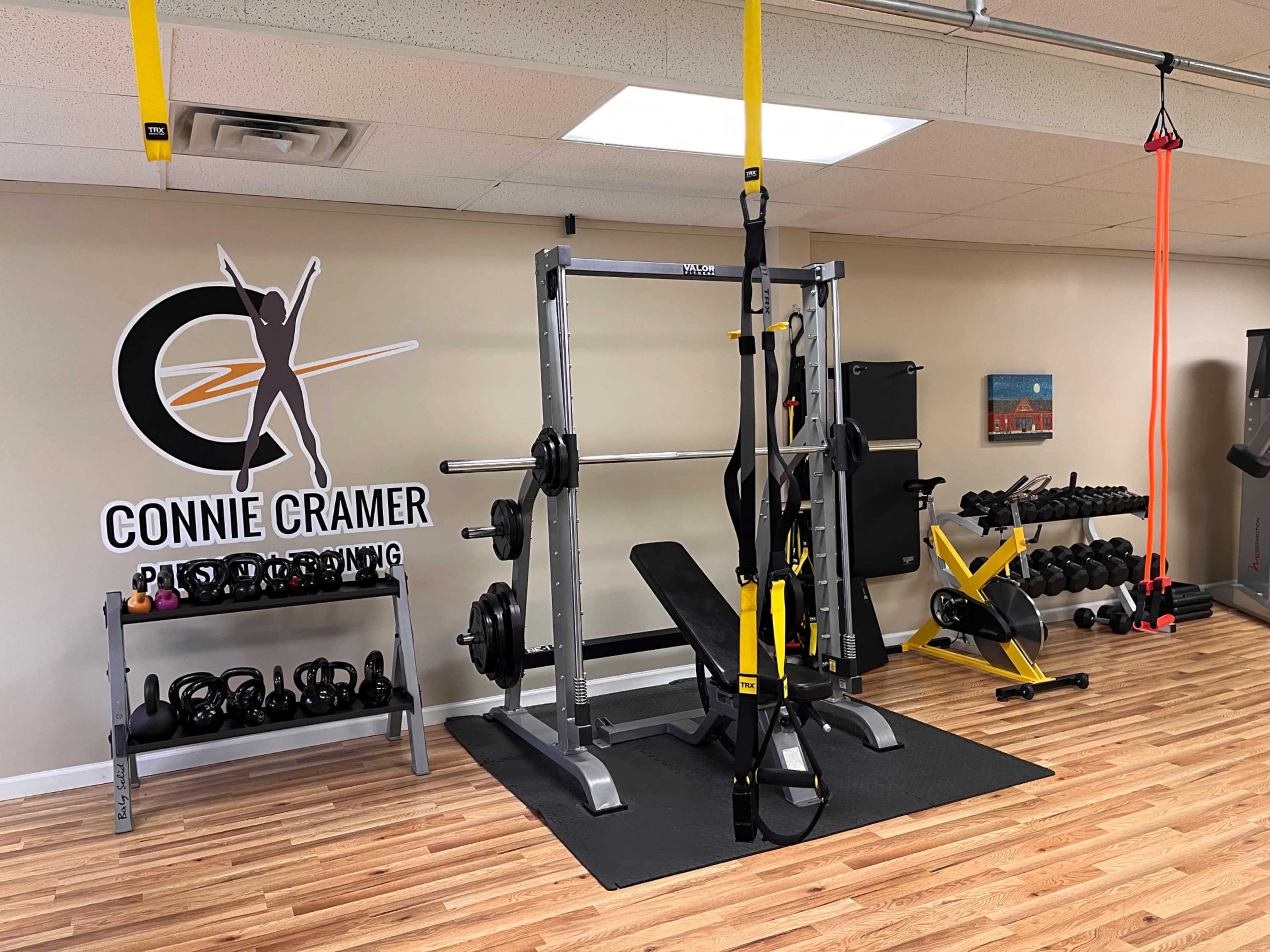 A fitness studio featuring weightlifting equipment, resistance bands, and a rack of dumbbells against a branded wall.