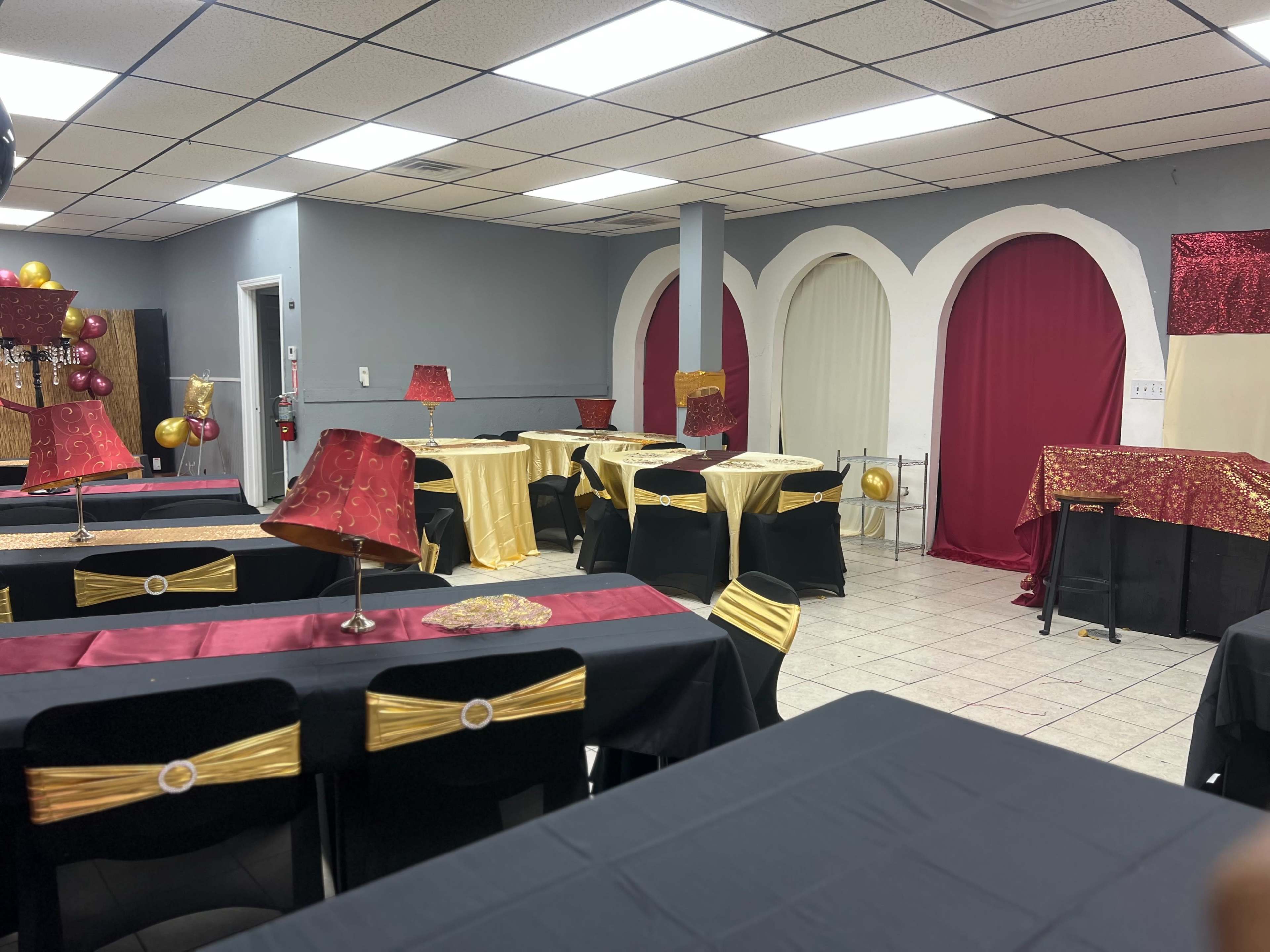 The room features tables with black and gold tablecloths, decorated with red accents, and has a backdrop of gold and burgundy curtains.