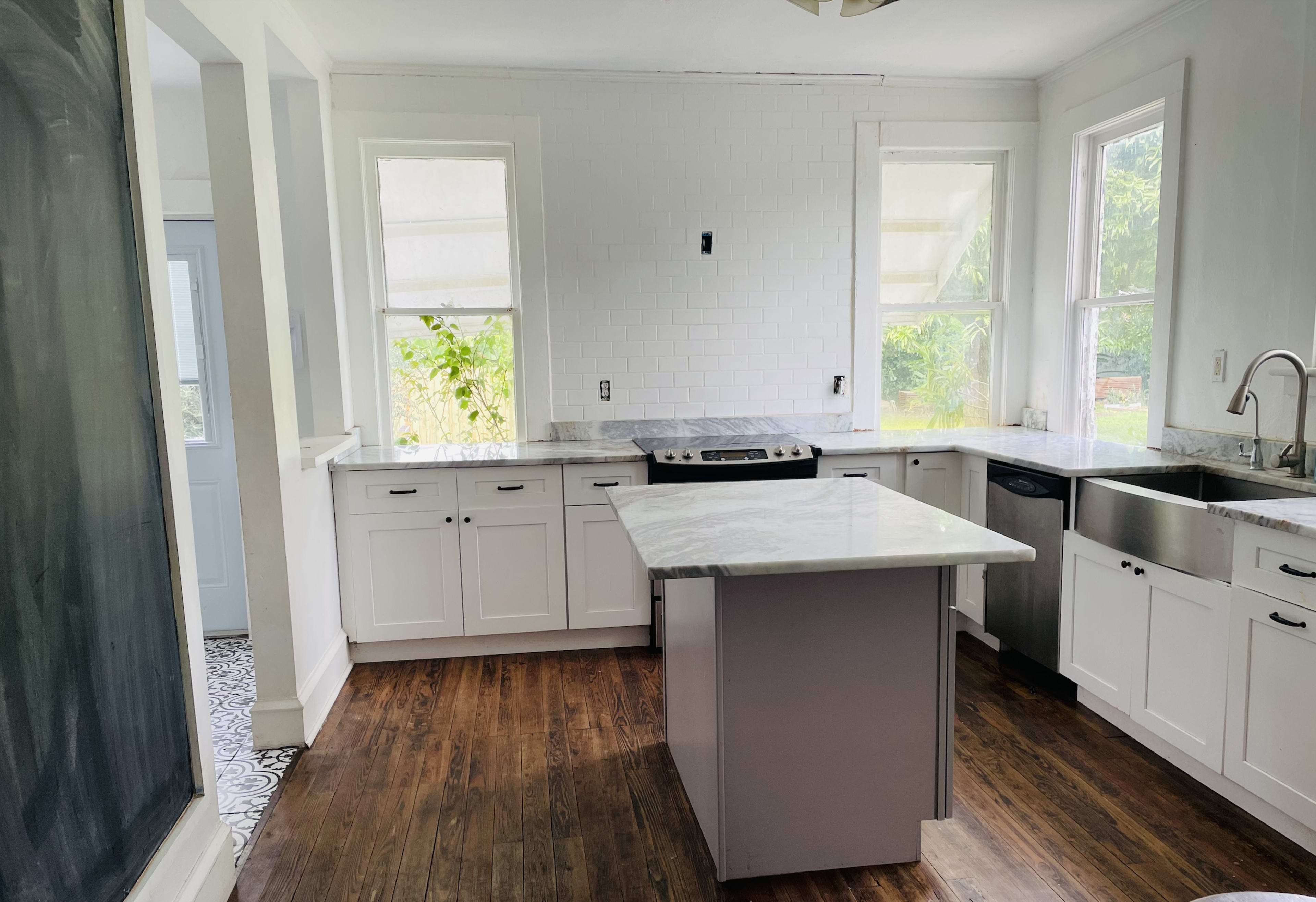 The image shows a modern kitchen with white cabinets, a large island, and natural light coming through multiple windows.