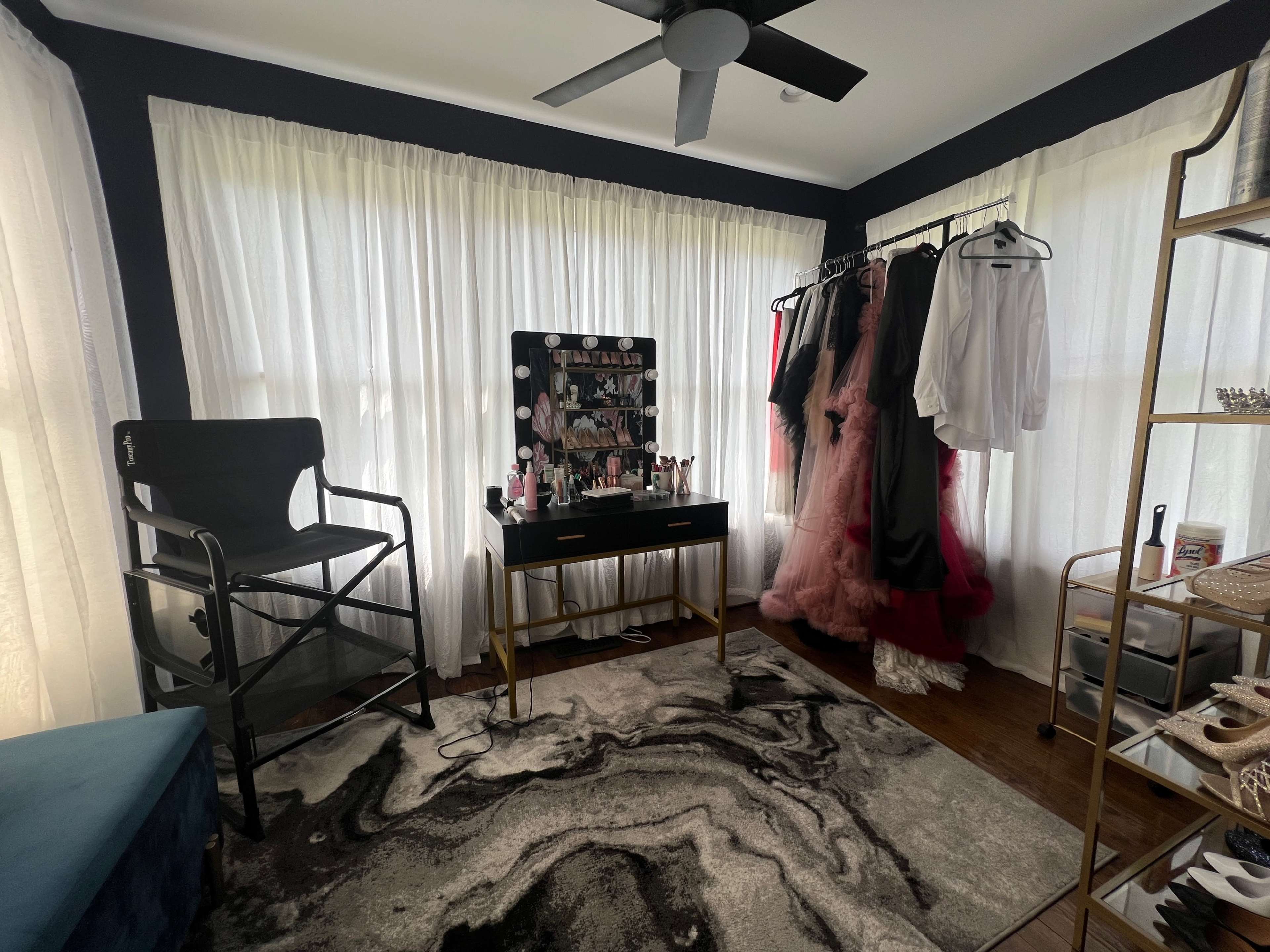 A bright room featuring a dressing area with a vanity, a clothing rack displaying various outfits, and a large area rug on the floor.