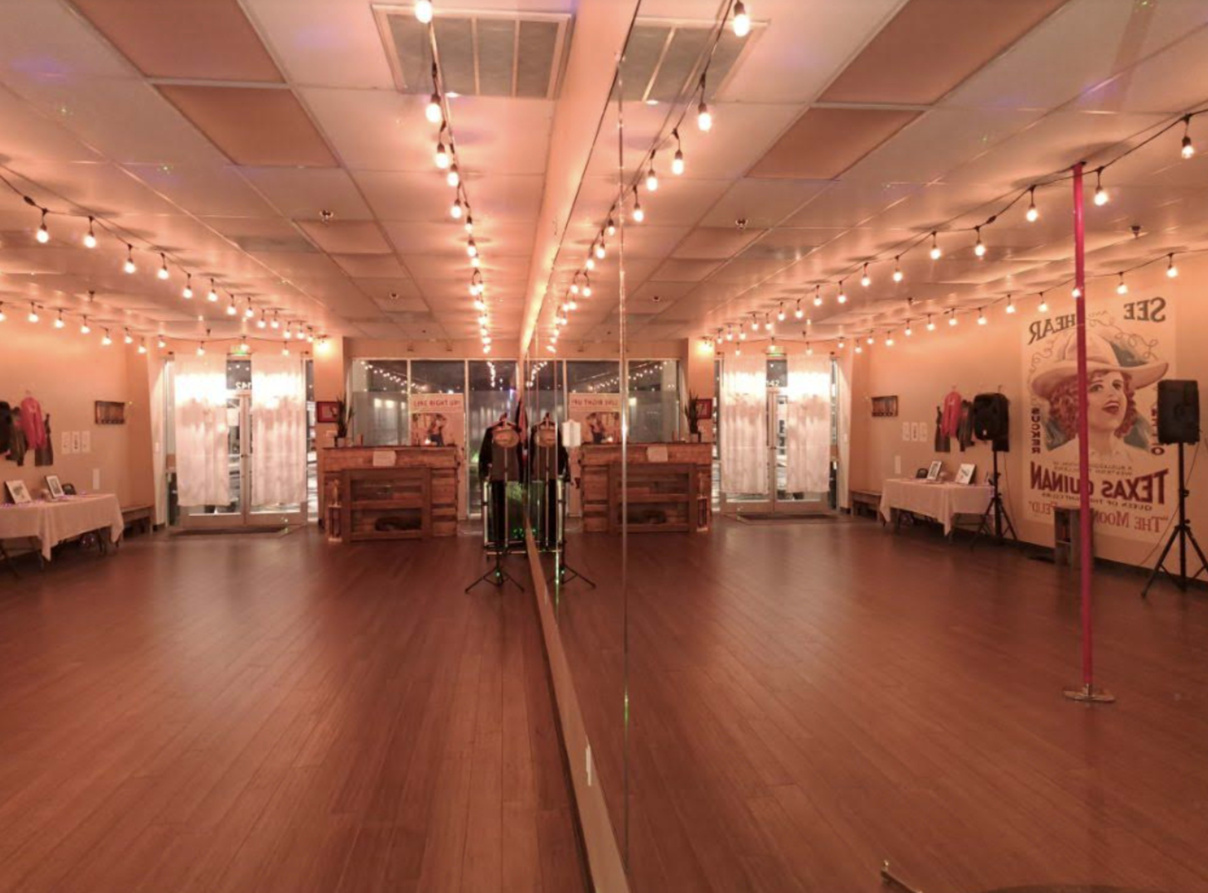 A spacious dance studio with mirrored walls, wooden flooring, and decorative string lights.