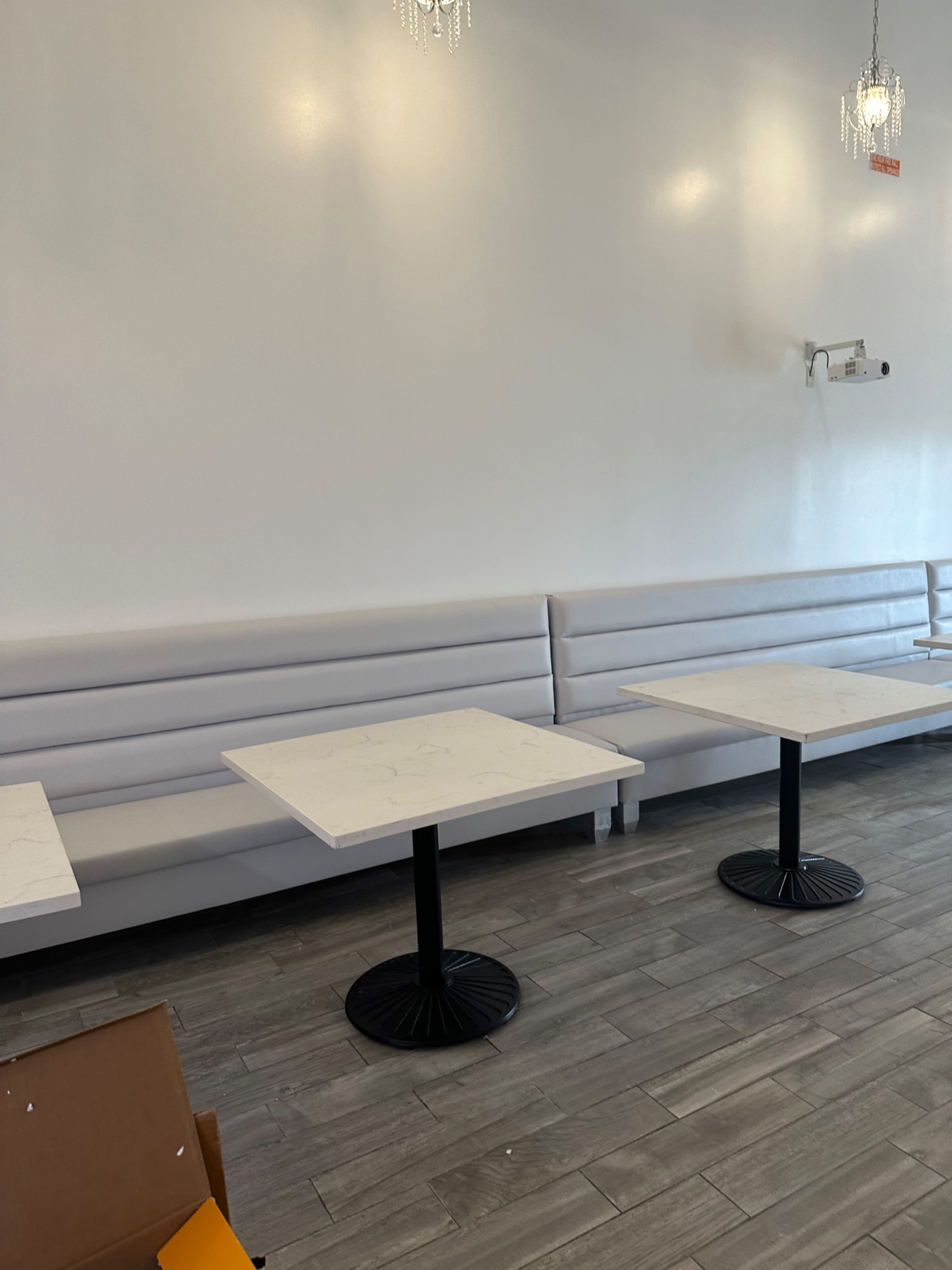 A sparsely furnished restaurant interior with white walls, marble-topped tables, and gray seating along one side.