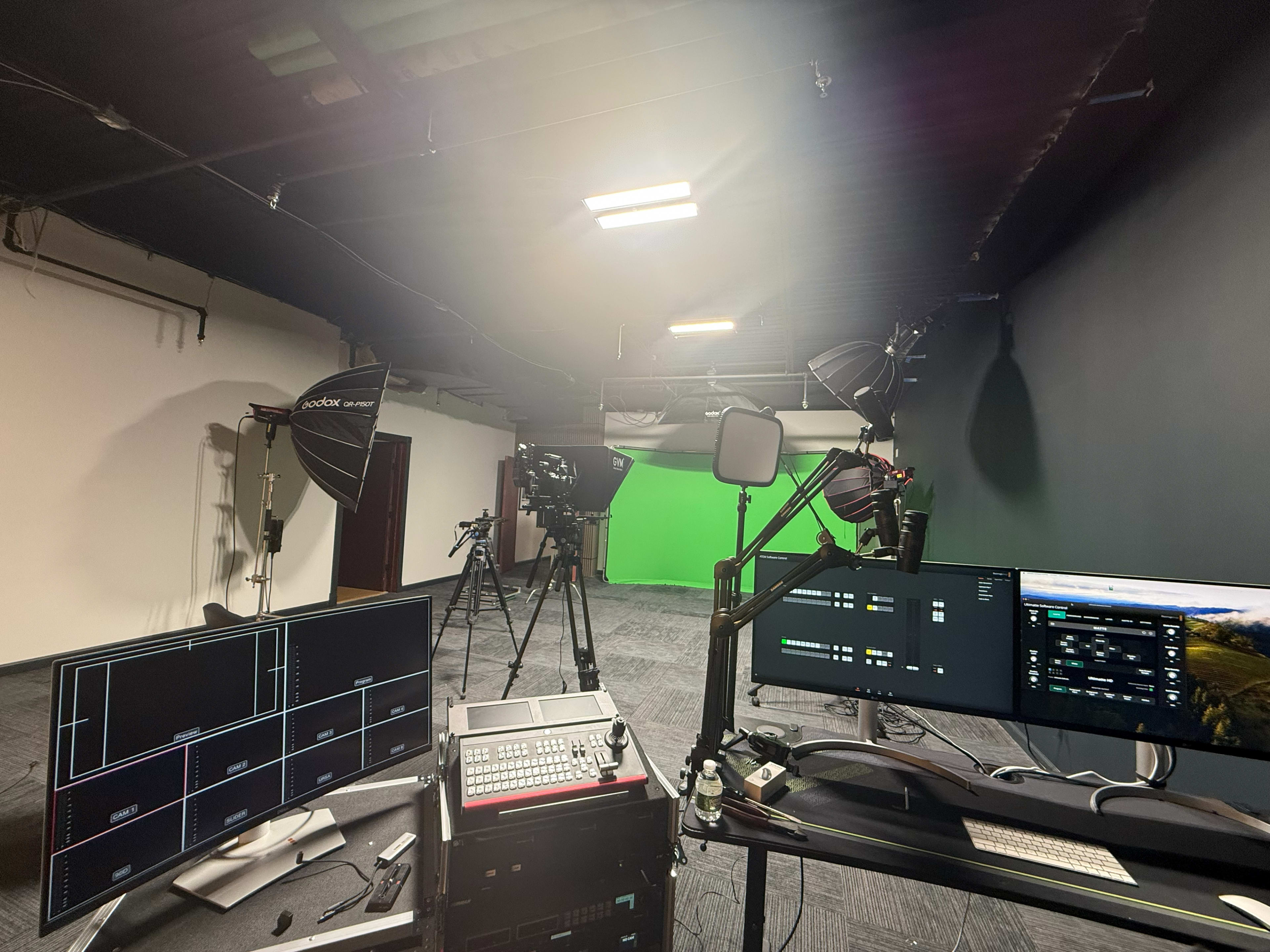 The image shows a video production setup featuring multiple screens, microphones, and lighting equipment in a studio with a green backdrop.