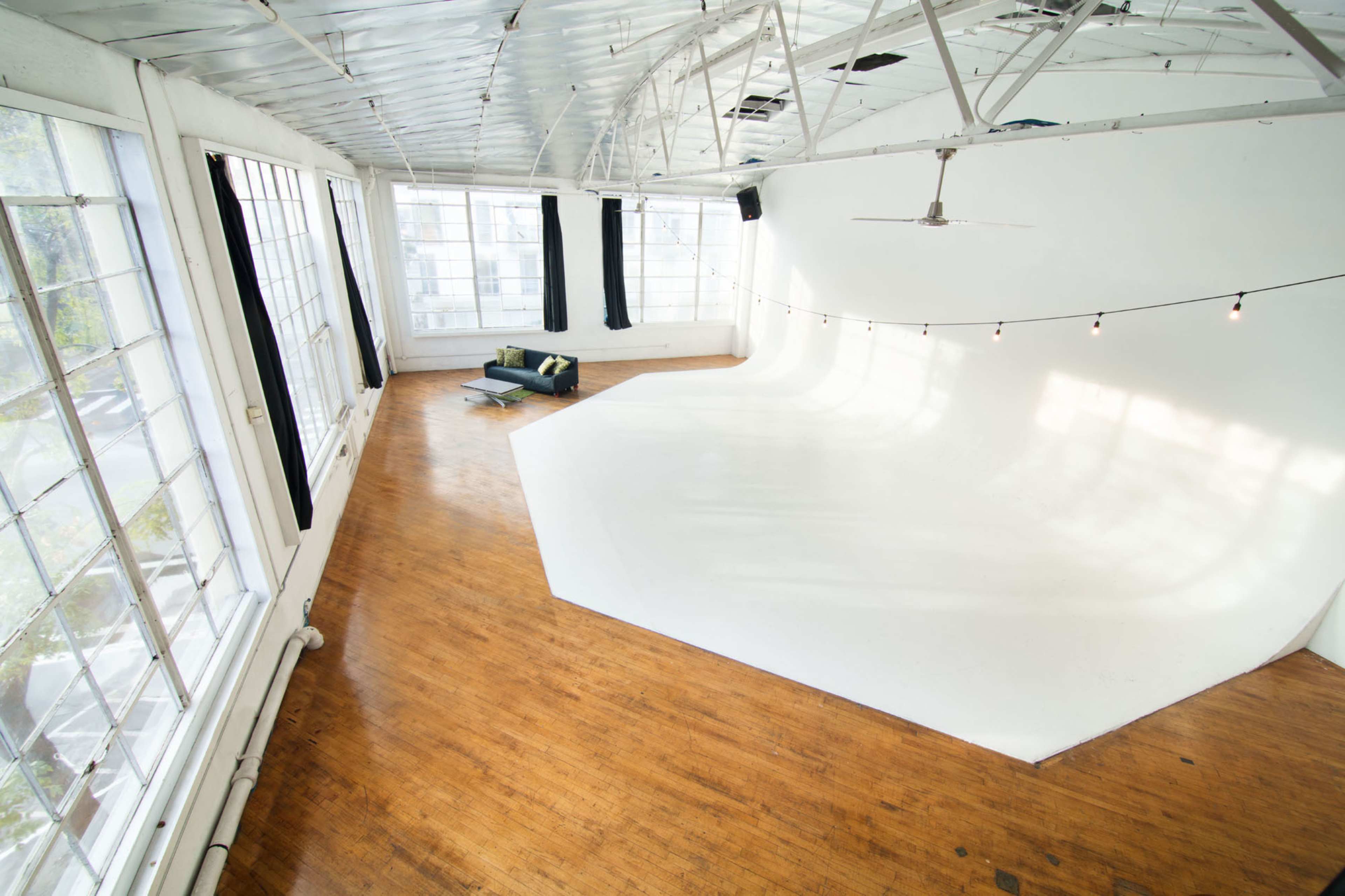 A spacious studio features large windows, wooden flooring, and a curved white backdrop.