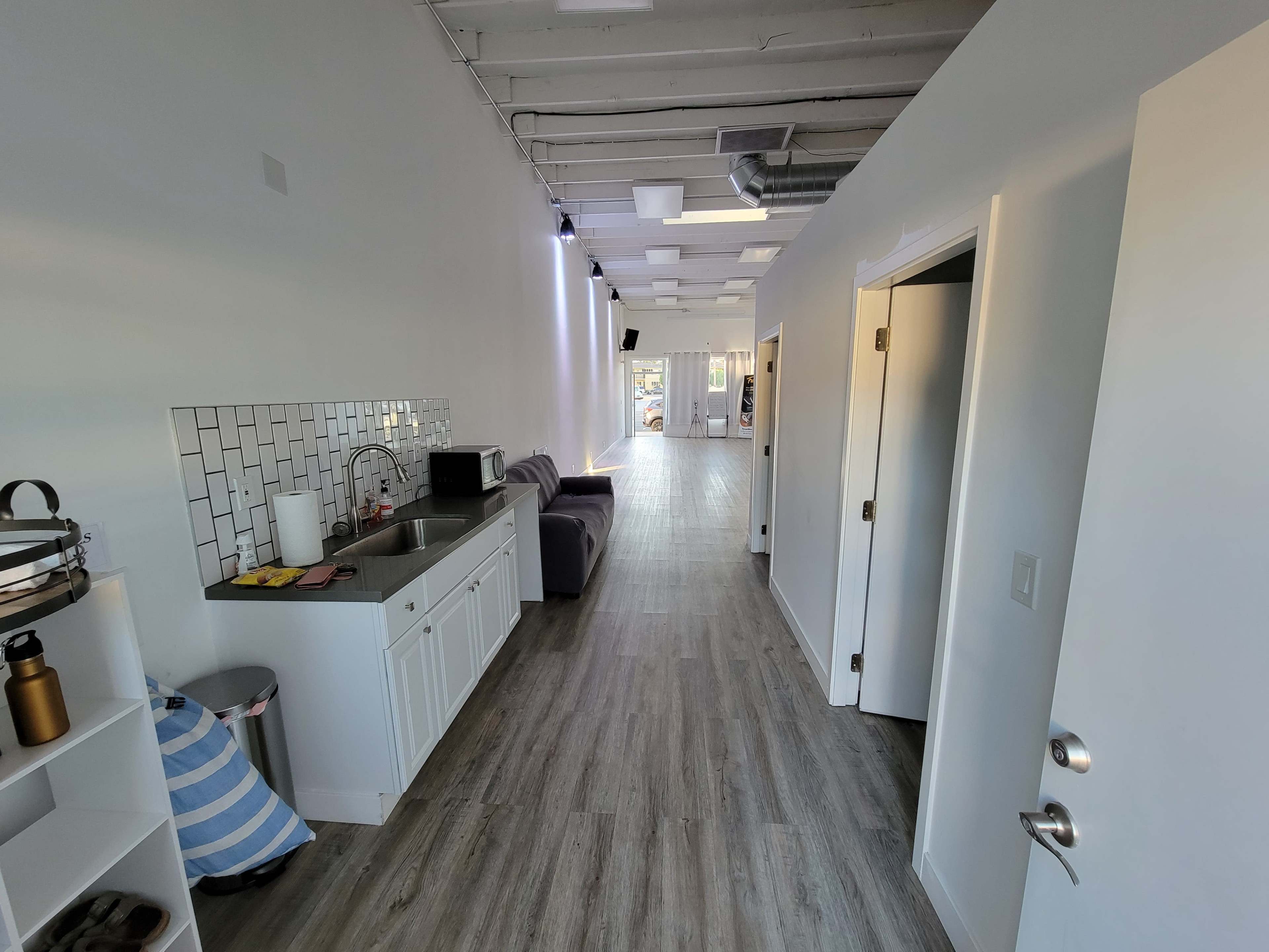 The image shows a modern corridor with a kitchen area on the left, hardwood flooring, and doors leading to different rooms.