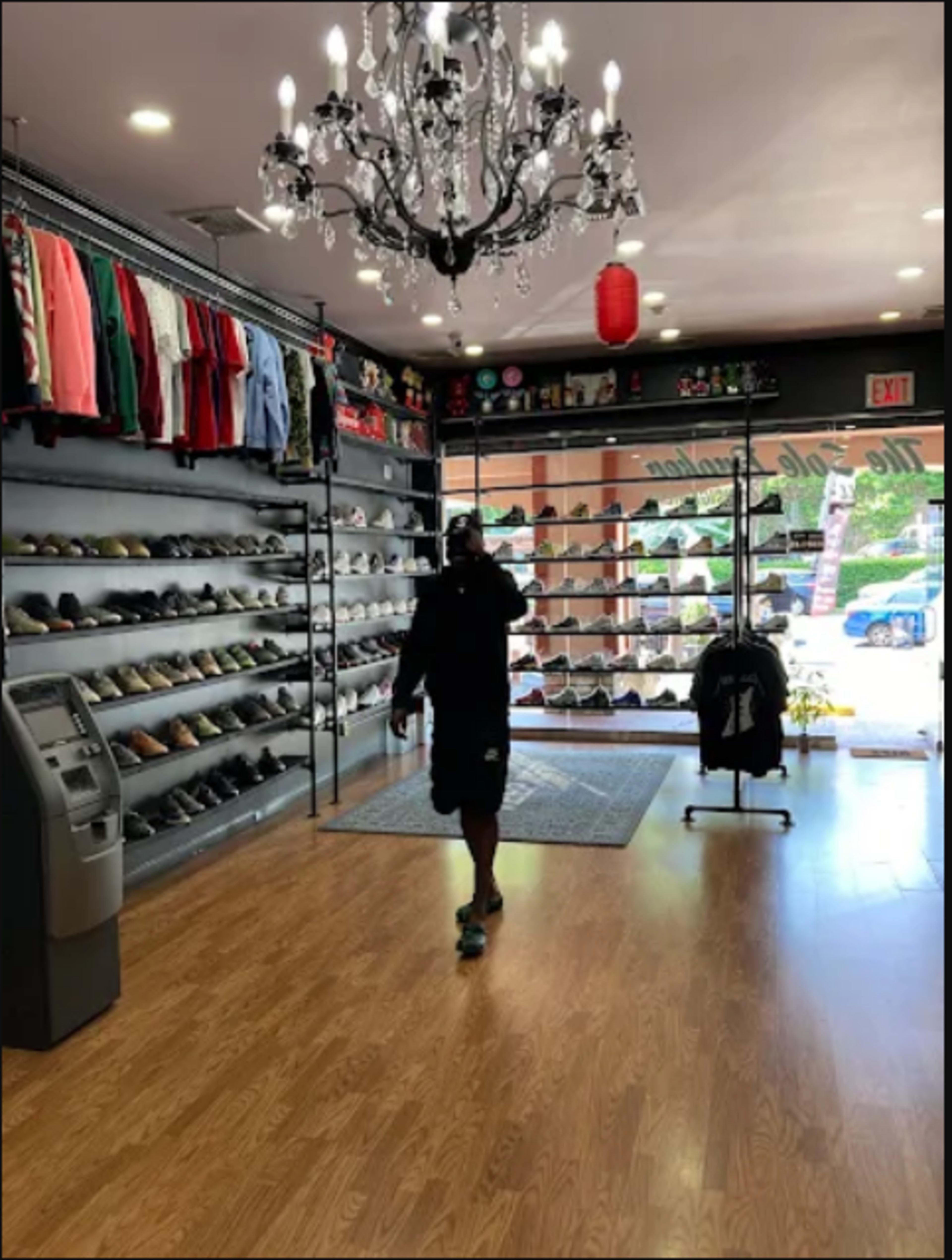 A person walks through a shoe store lined with various footwear displays and clothing racks, beneath a chandelier.
