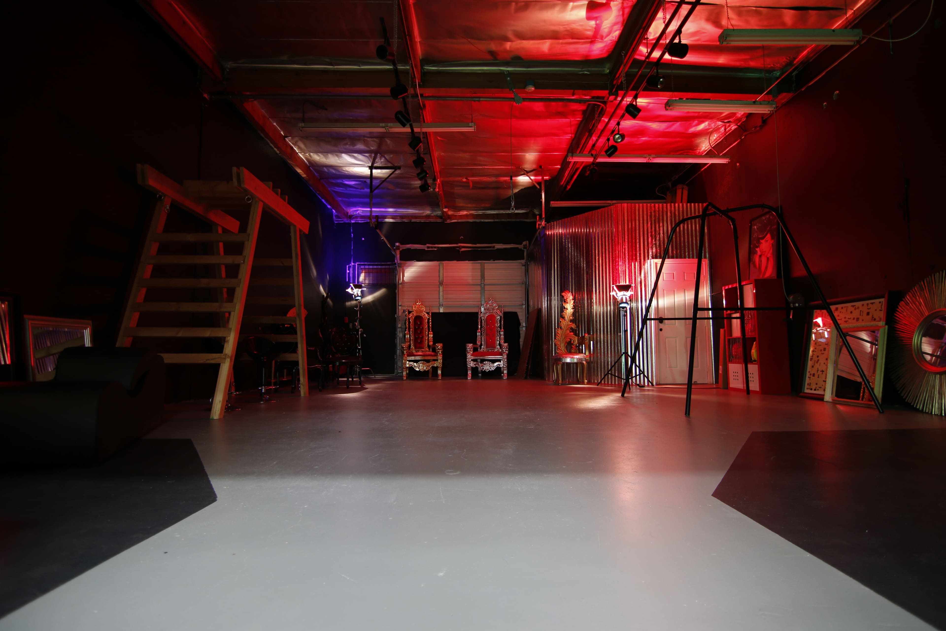 A spacious, dimly lit studio with colorful lighting, a staircase, and various pieces of furniture and decor arranged throughout.