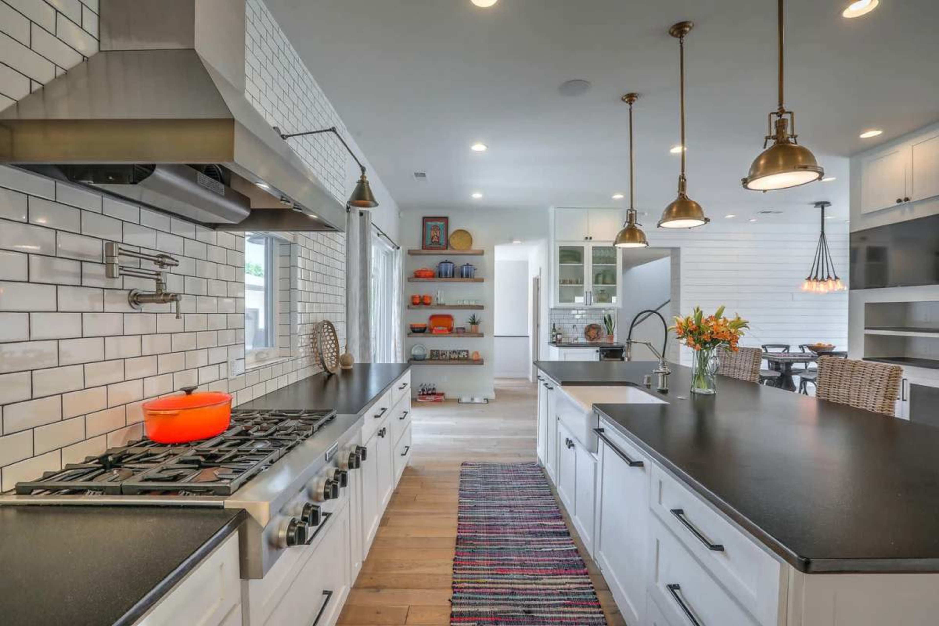 The image shows a modern kitchen with white cabinetry, a stainless steel gas stove, black countertops, and pendant lights hanging over two island counters.