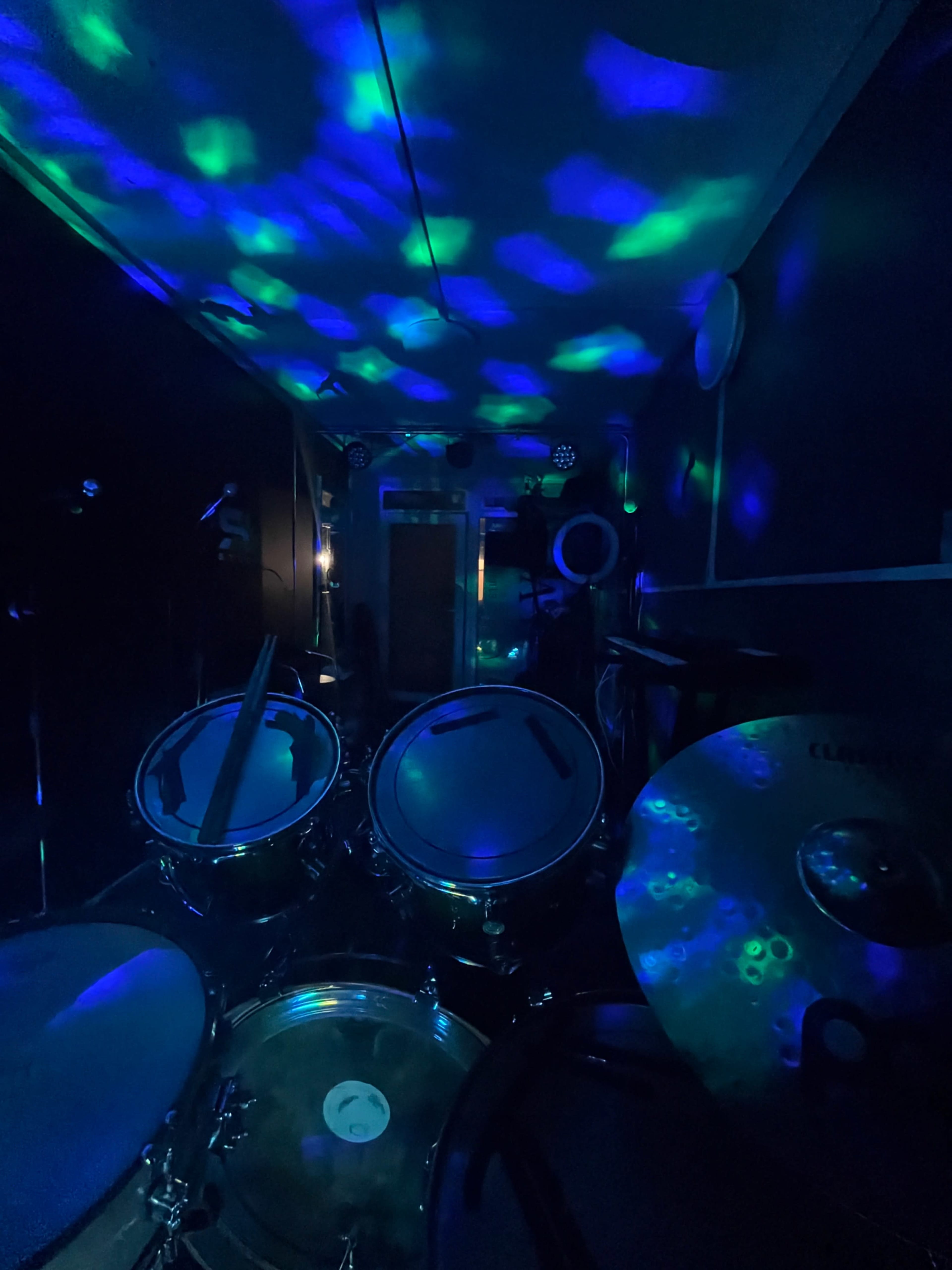 A drum set is positioned in a dimly lit room with colorful lights casting patterns on the walls and ceiling.