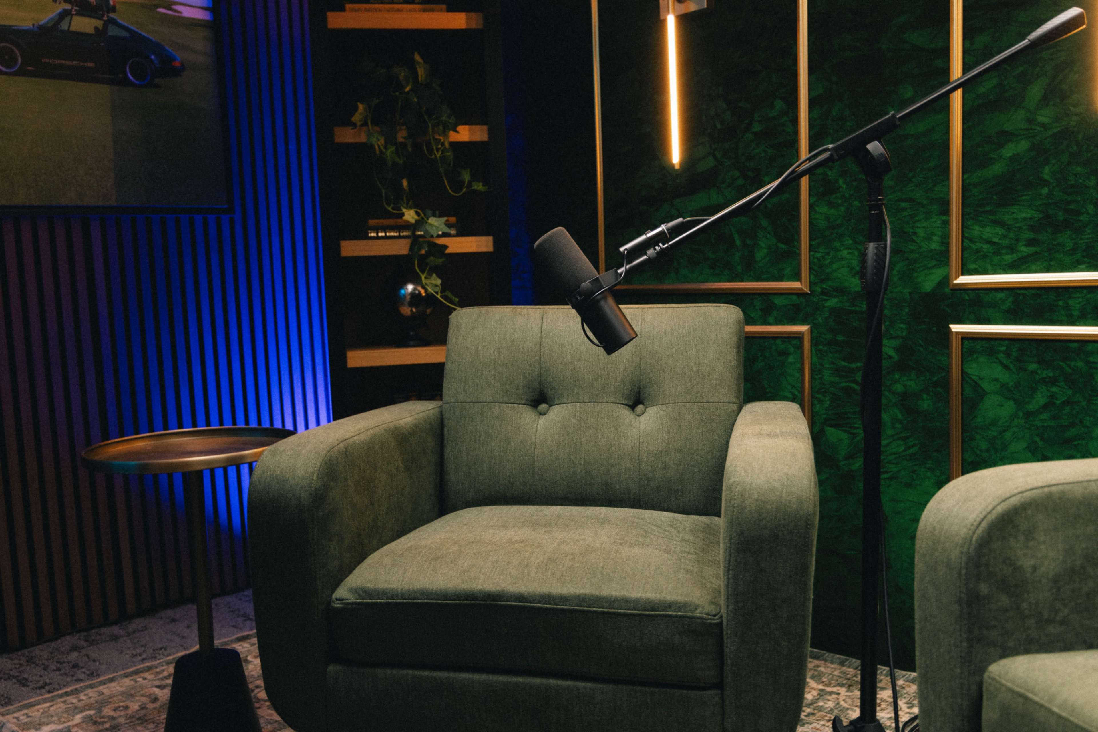 The image shows a stylish green armchair beside a small round table, with a microphone positioned nearby in a well-lit studio setting.