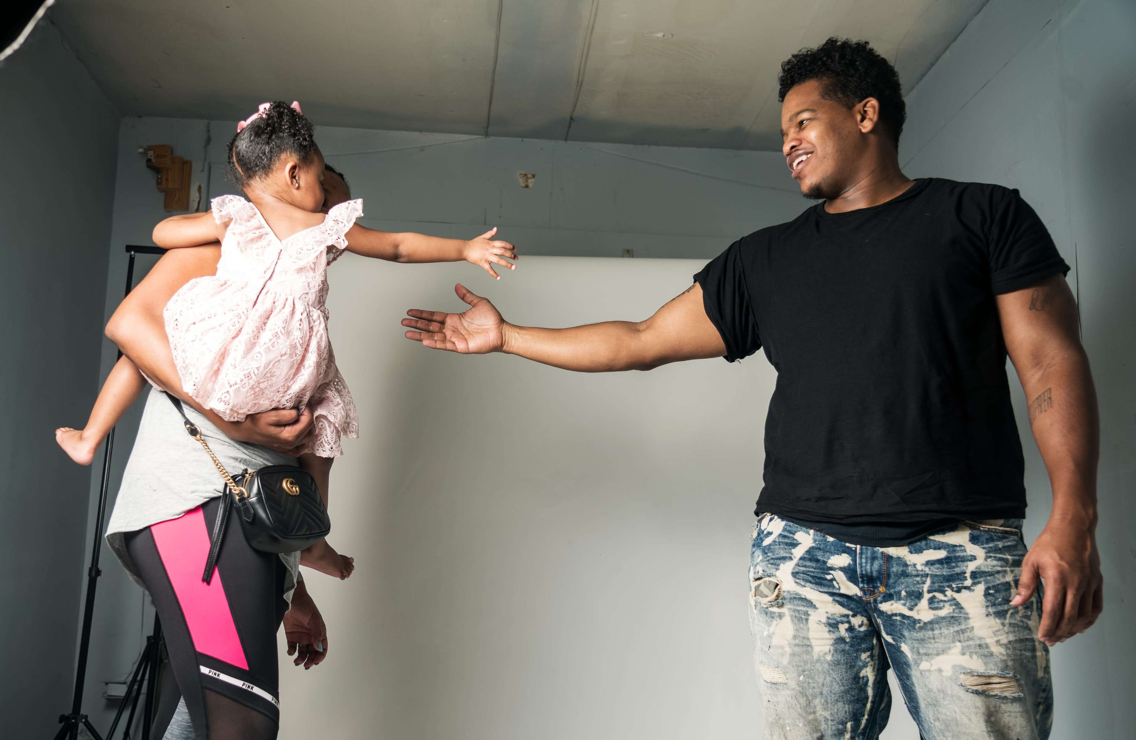 A man reaches out to a toddler being held by a woman in a photography studio.
