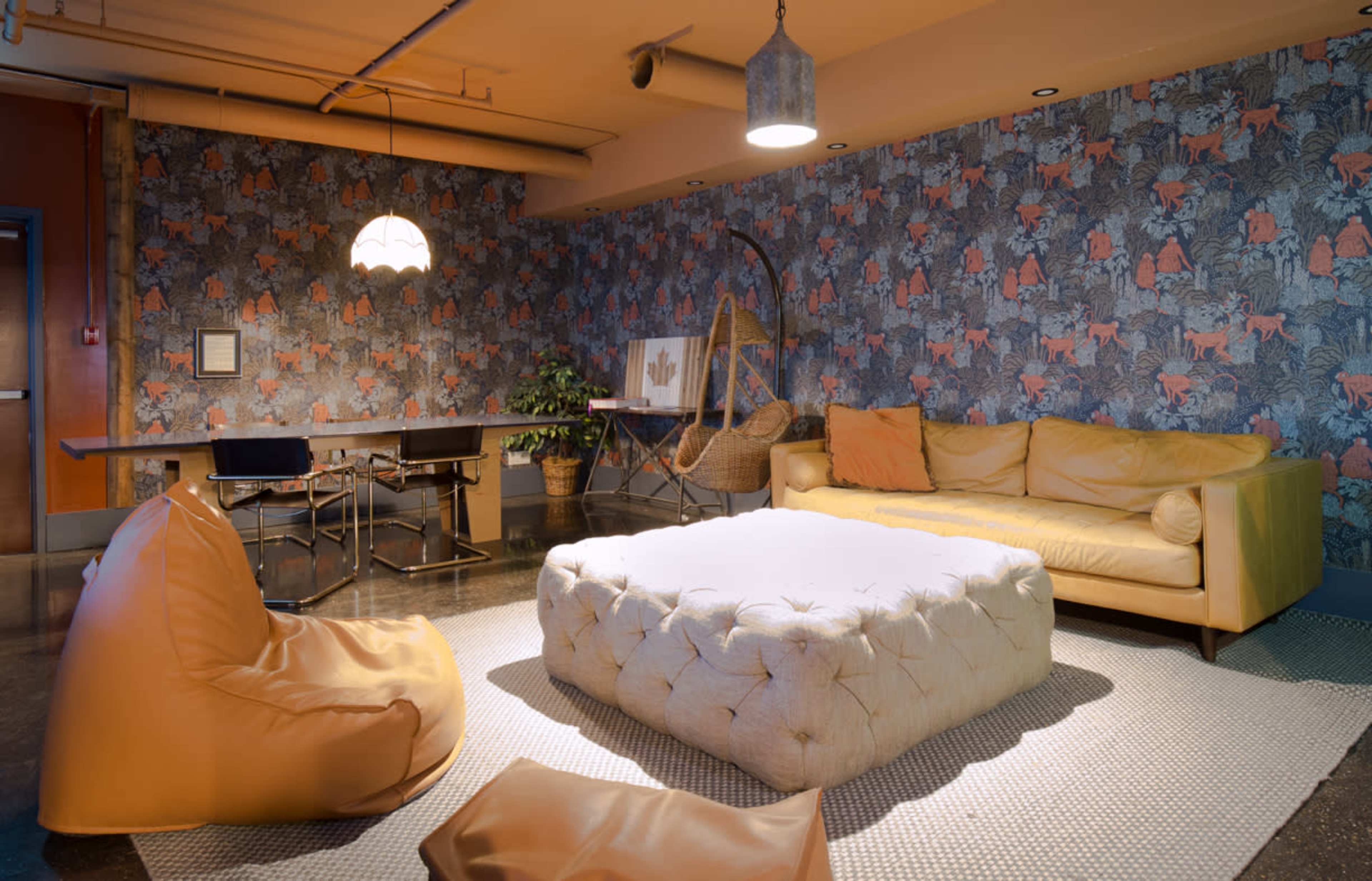 A cozy lounge area features a tufted coffee table, yellow leather sofa, bean bag chairs, and a wallpaper with a vibrant animal-themed pattern.