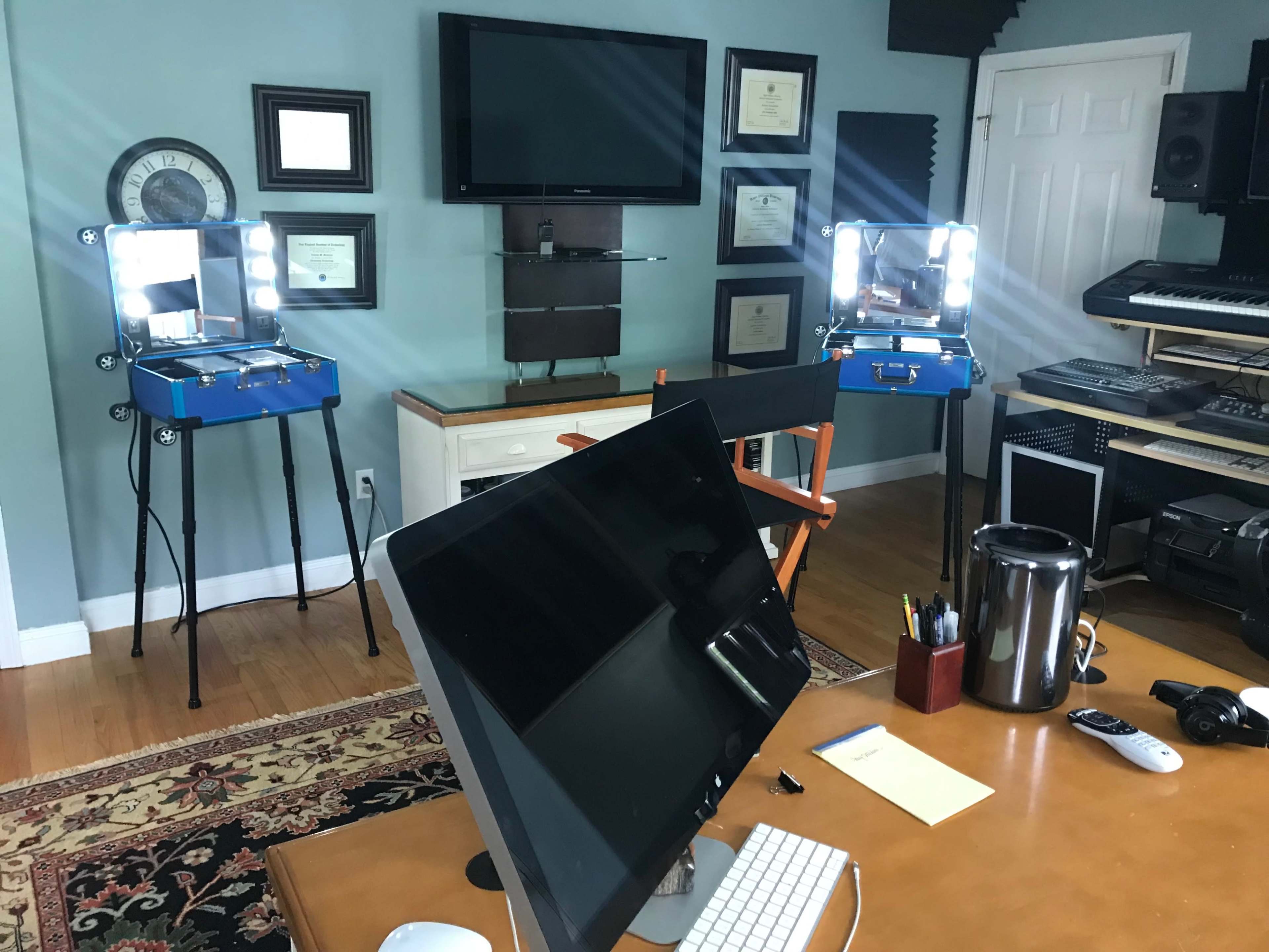 A room with a large monitor, two illuminated makeup stations, a desk, and various musical equipment.