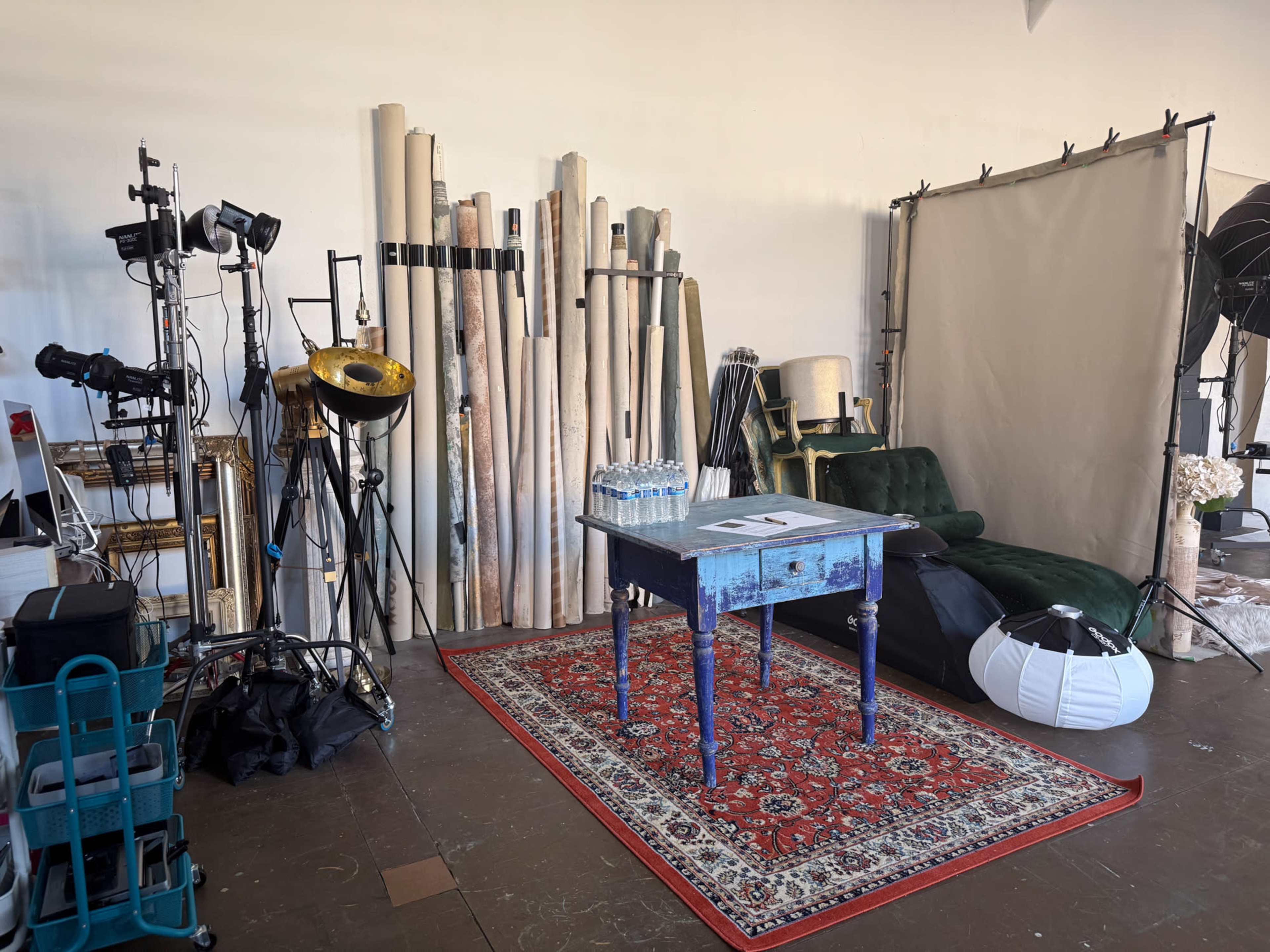 The image shows a photography studio with various backdrops, lighting equipment, a table, and a green couch arranged in a corner.