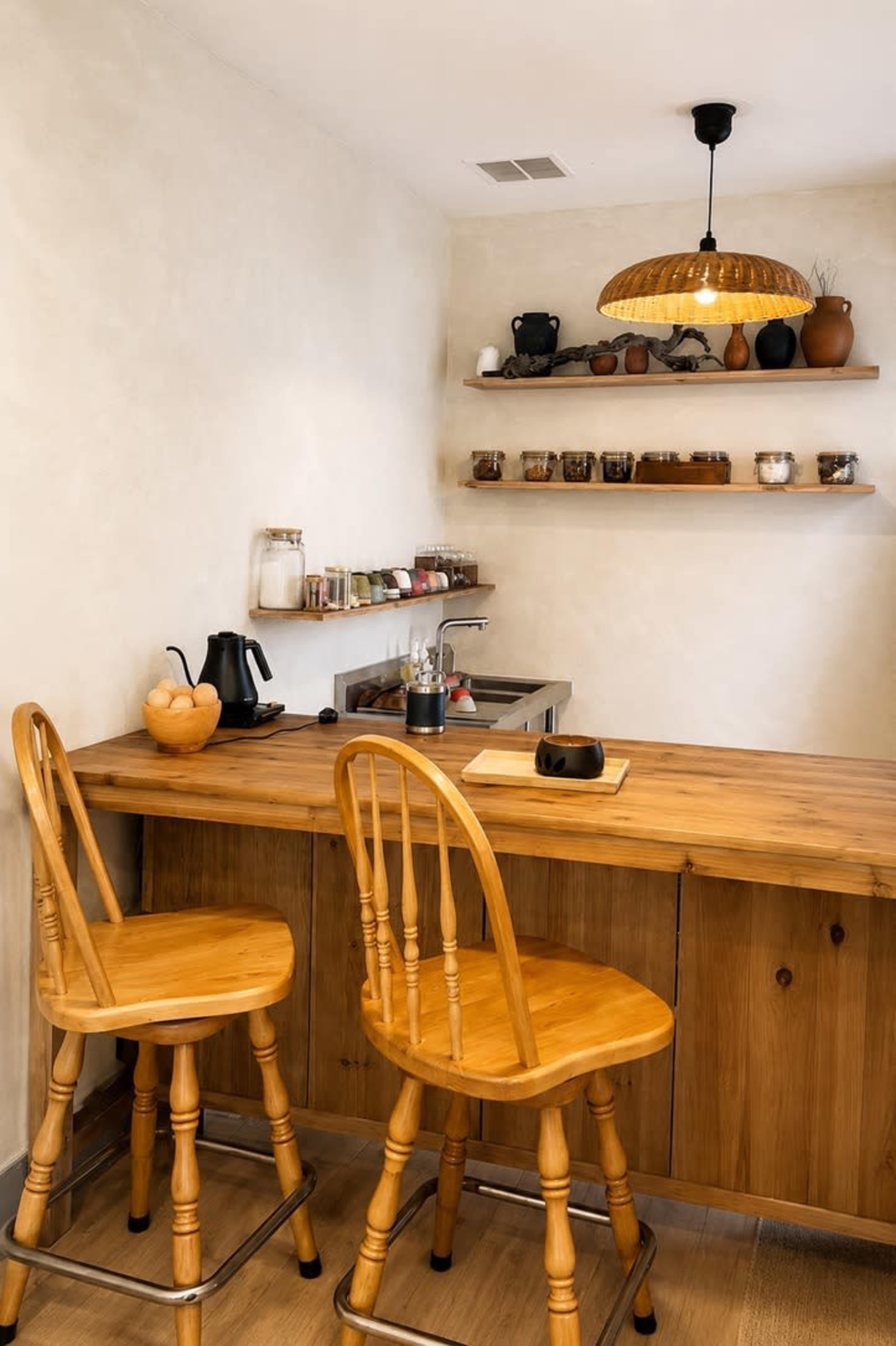 The image shows a modern kitchen with a wooden counter, two wooden chairs, and shelves displaying various ceramic pots and jars.