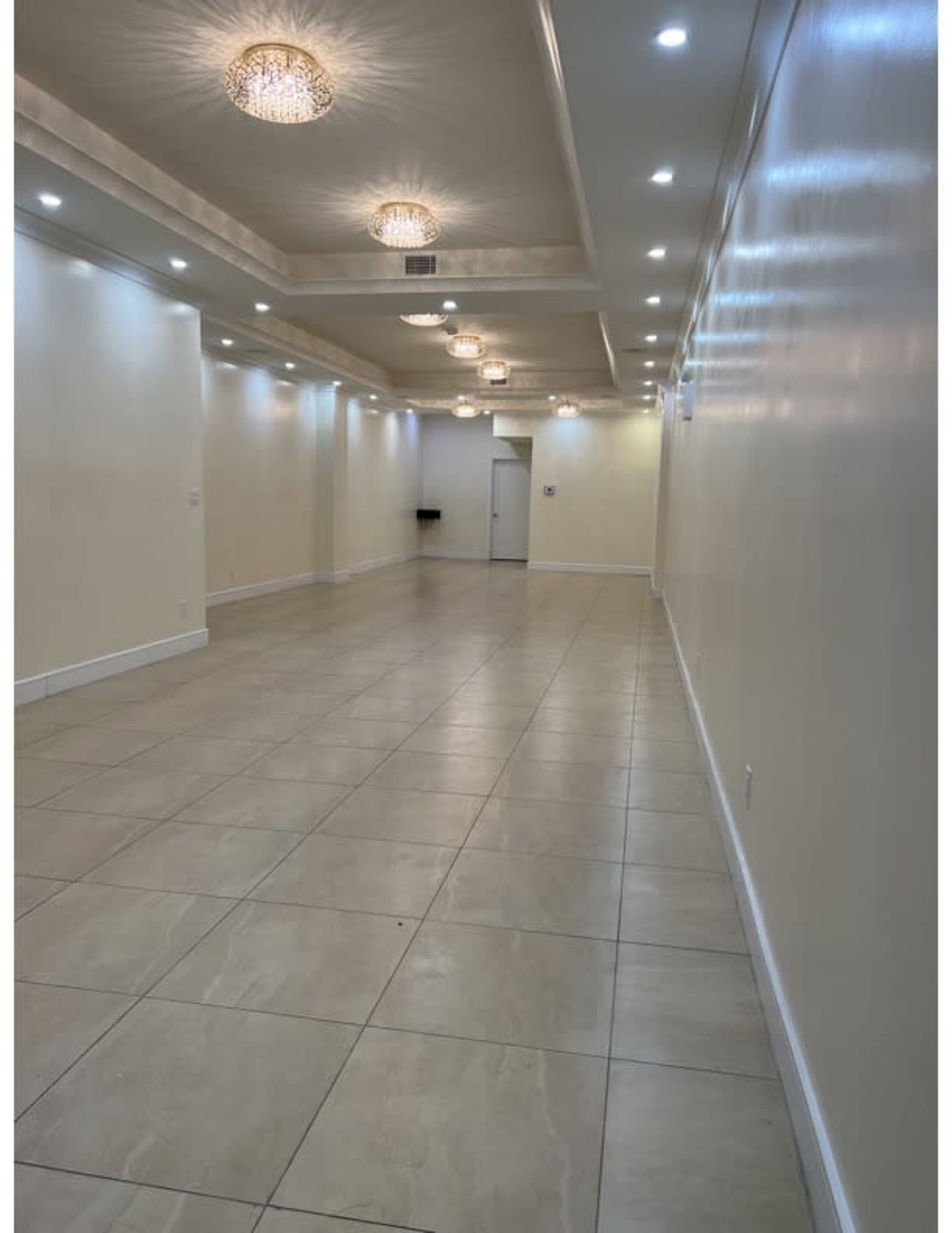 A well-lit, empty hallway with tiled flooring and decorative ceiling lights.