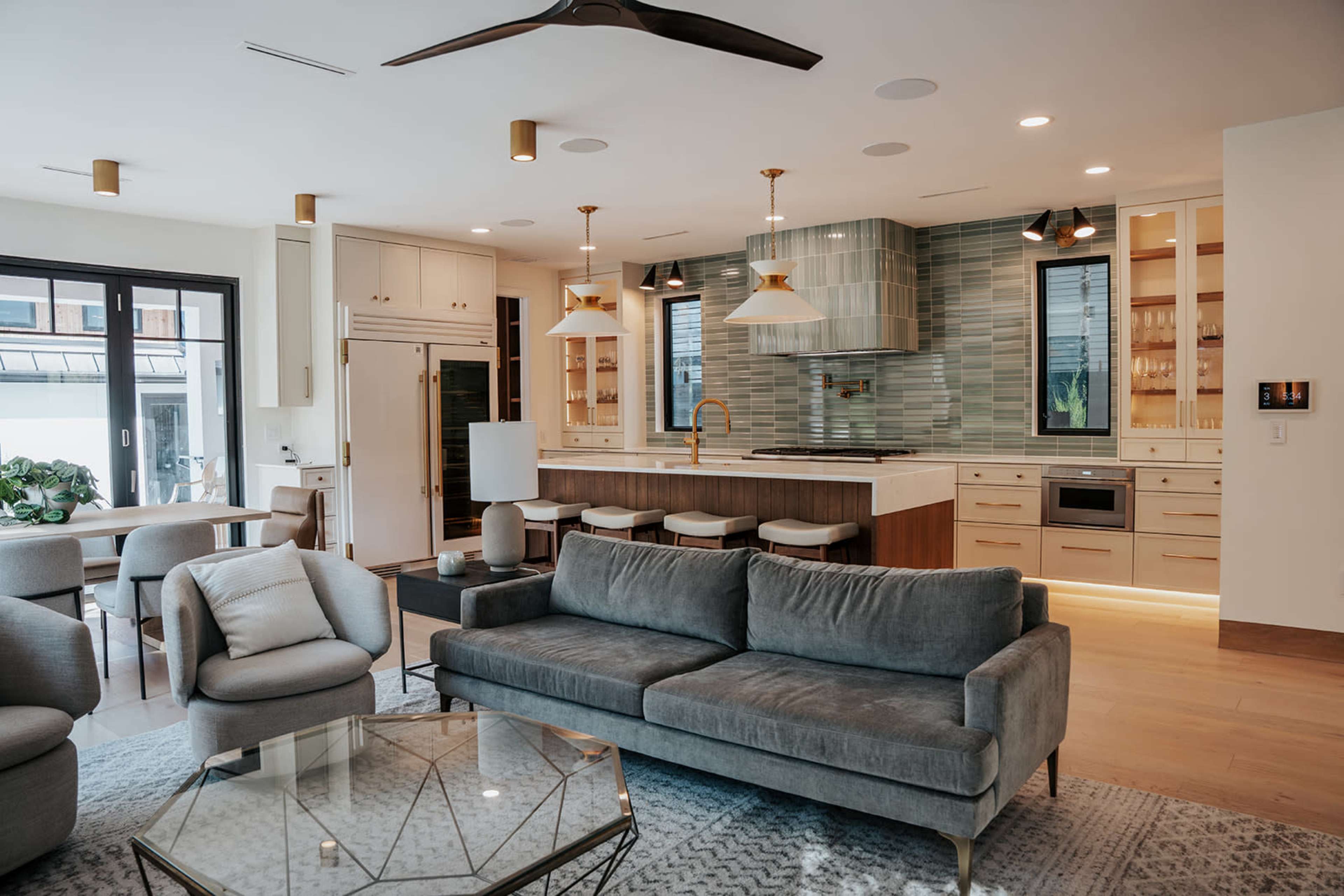 The image shows a modern living space with an open kitchen, featuring a gray sofa, a glass coffee table, and a dining area with a round table and chairs.