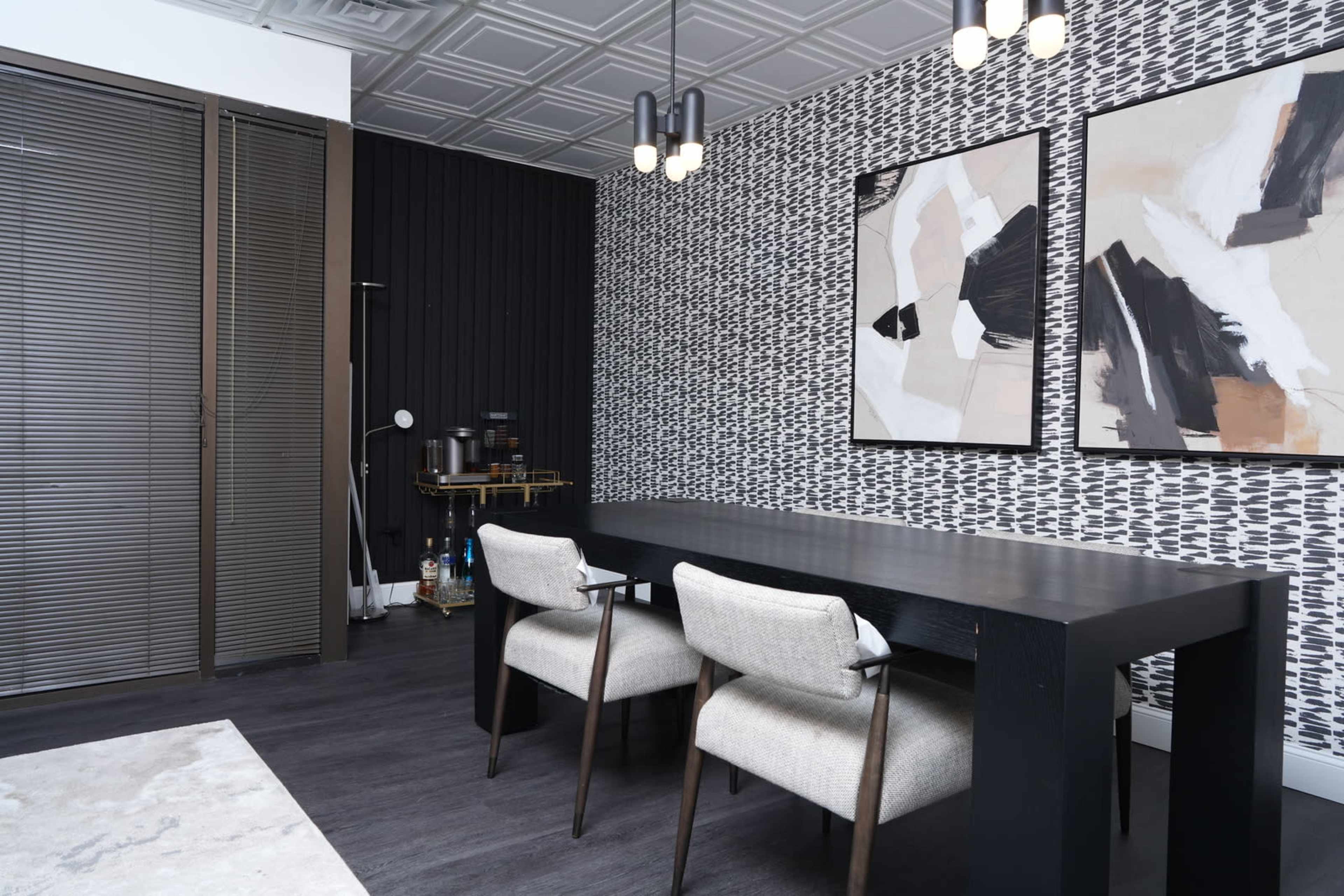 A modern room featuring a dark wood table with two upholstered chairs, wallpapered walls with abstract art, and a decorative shelving unit.