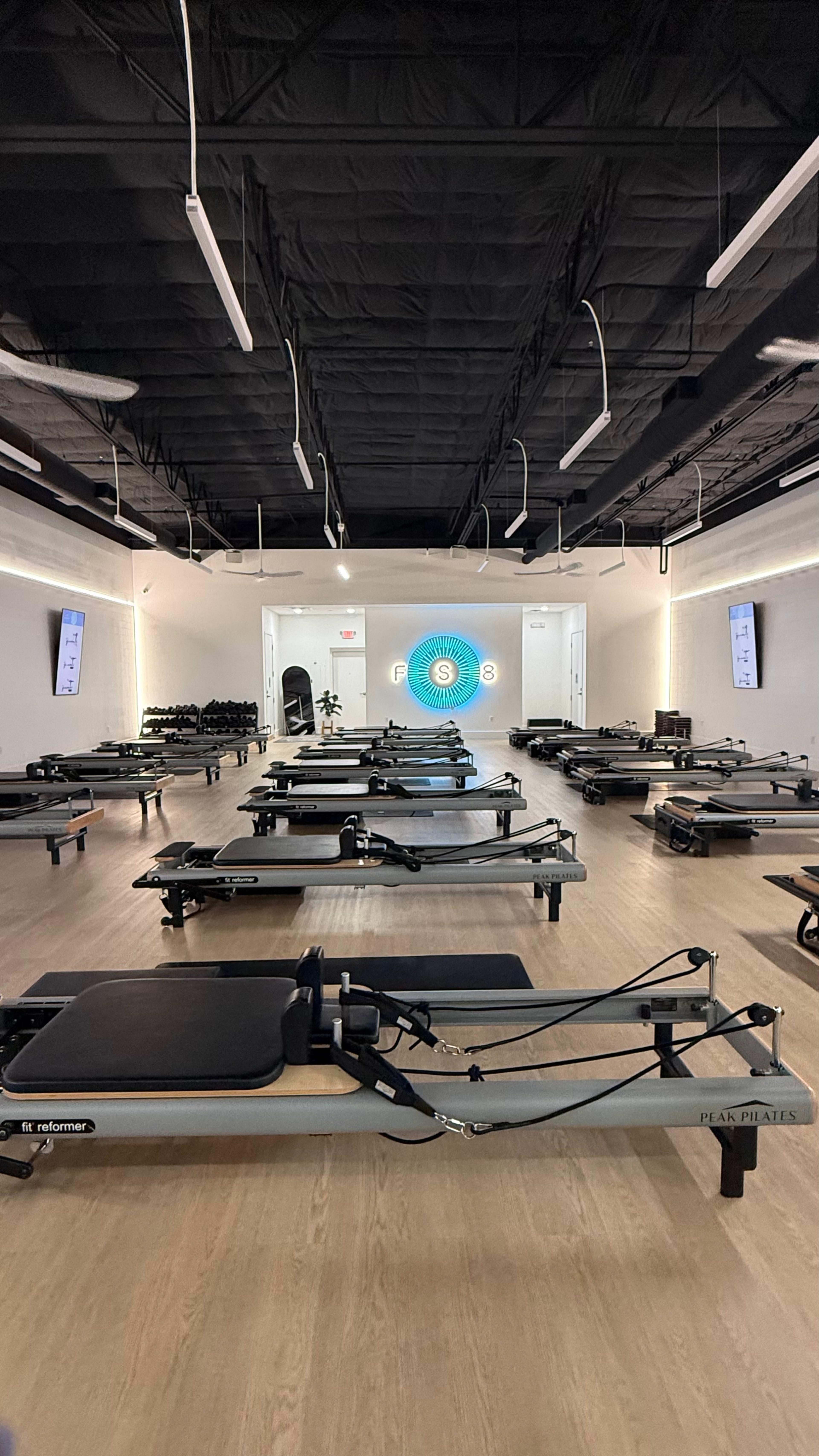 The image shows a well-lit Pilates studio filled with multiple reformer machines arranged neatly in rows.