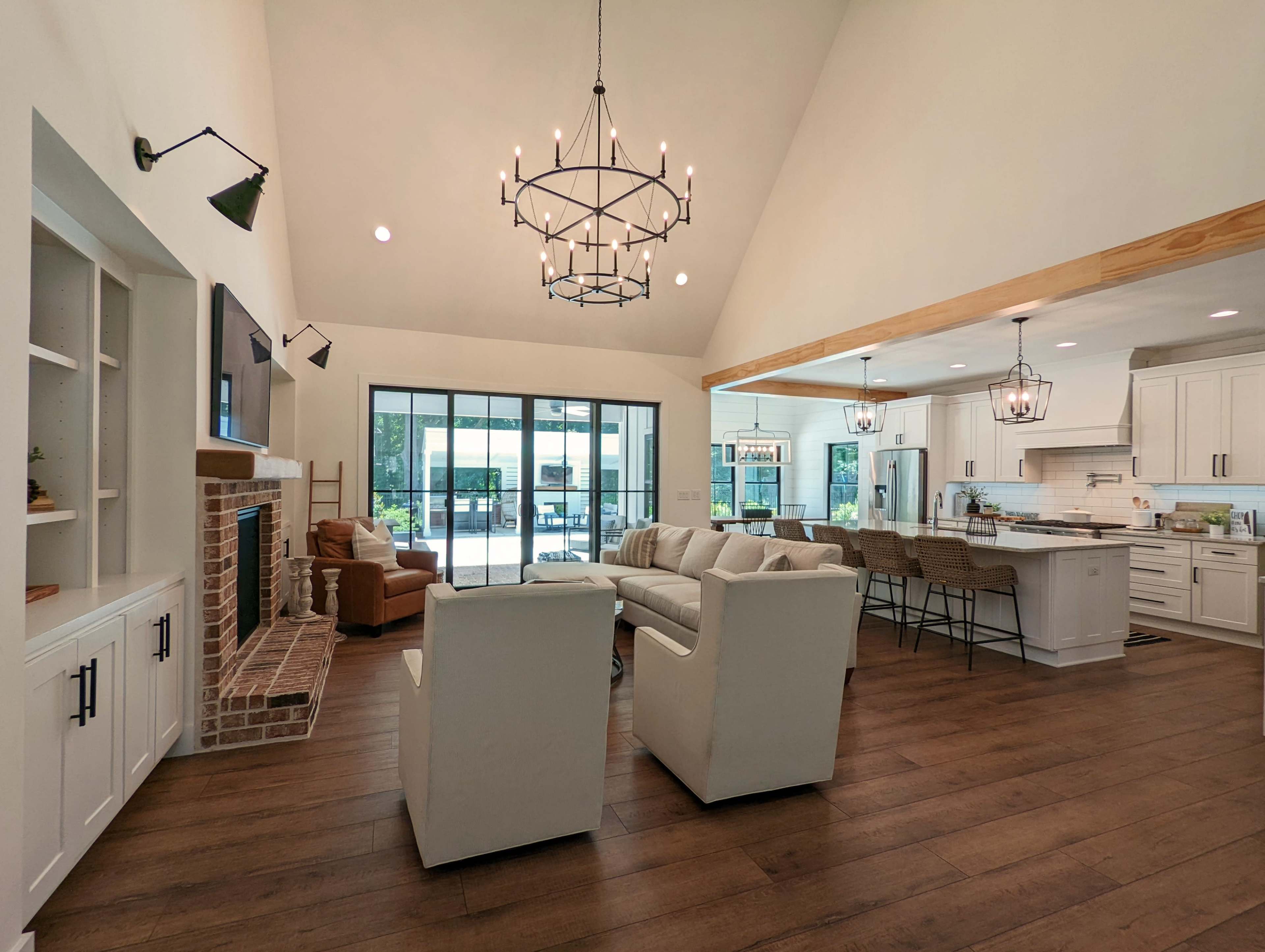 The image shows a spacious living area with a high ceiling, featuring a combination of a seating arrangement, a fireplace, and an open kitchen with bar seating.