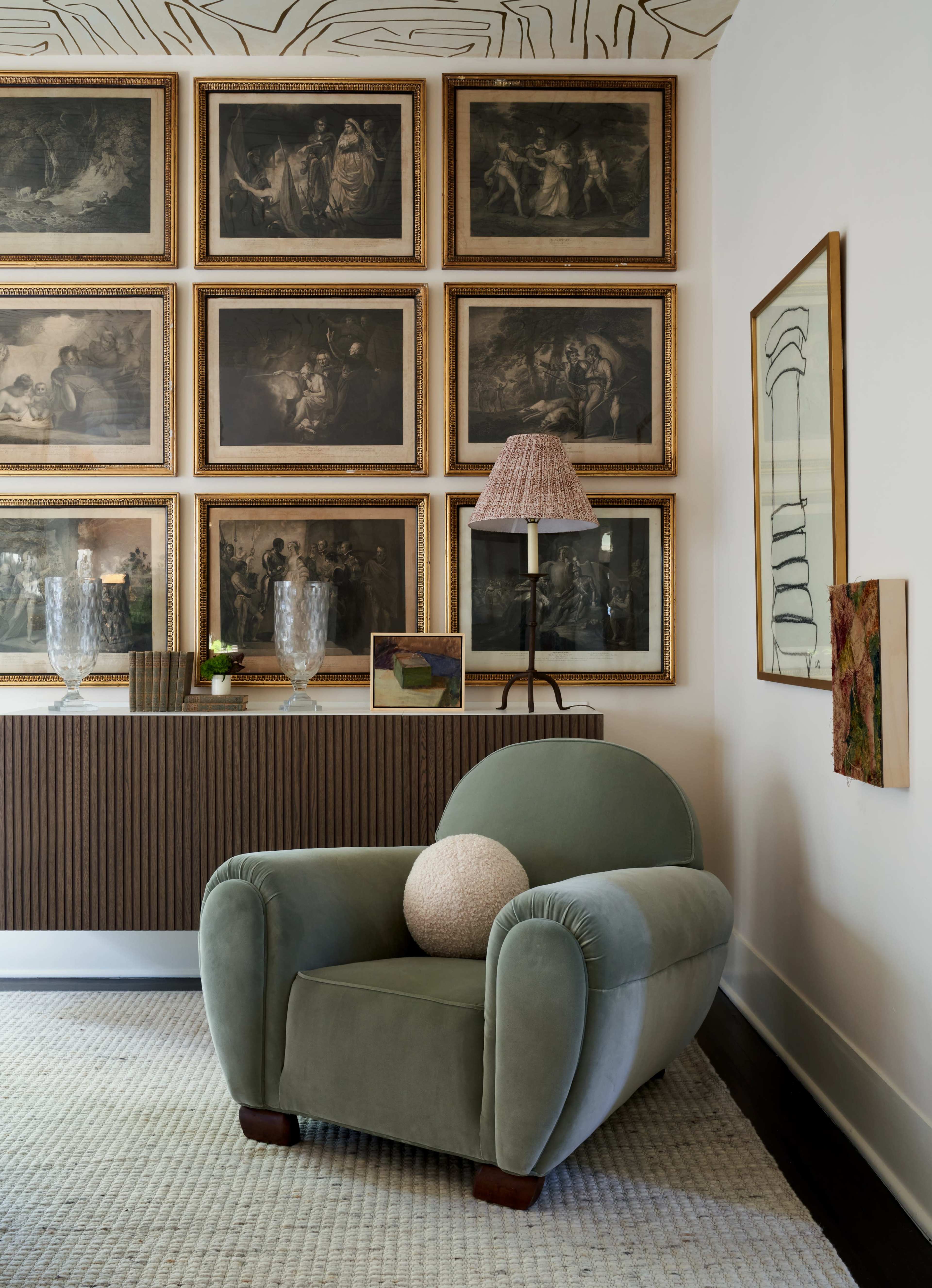 A green upholstered chair with a round cushion is positioned near a textured sideboard adorned with framed artworks and decorative items on a light-colored rug.