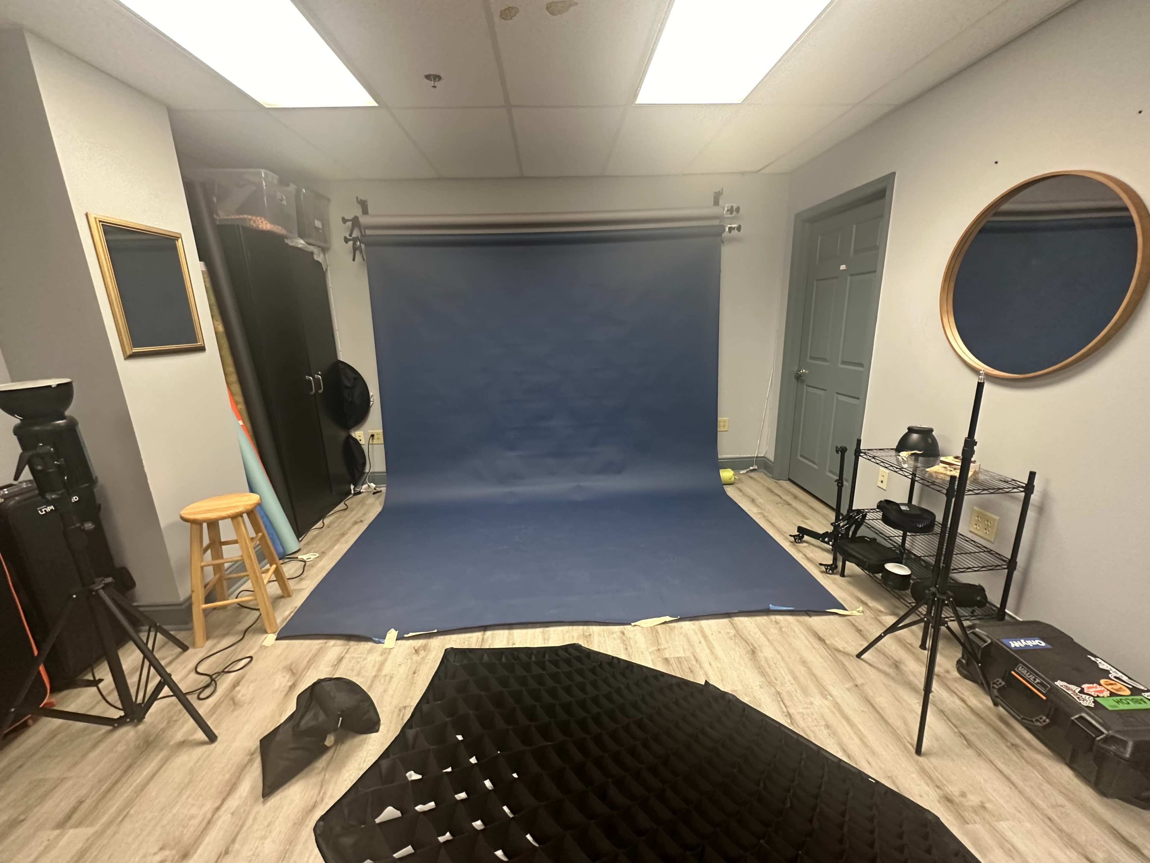 A photography studio with a blue backdrop, lighting equipment, and various props arranged on the floor.