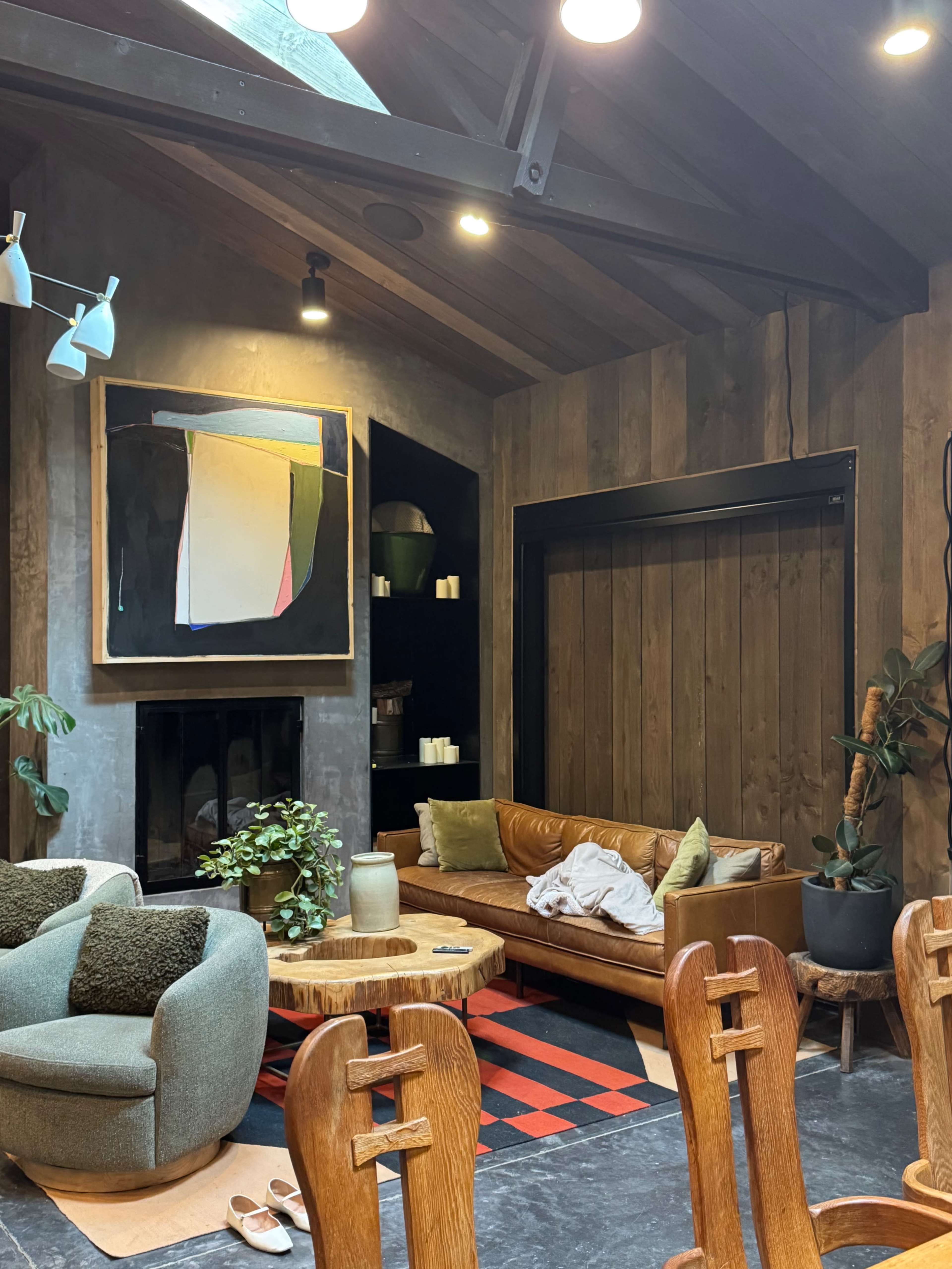 The image shows a cozy living room with a leather sofa, modern art on the wall, and wooden accents, featuring a variety of seating options and plants.