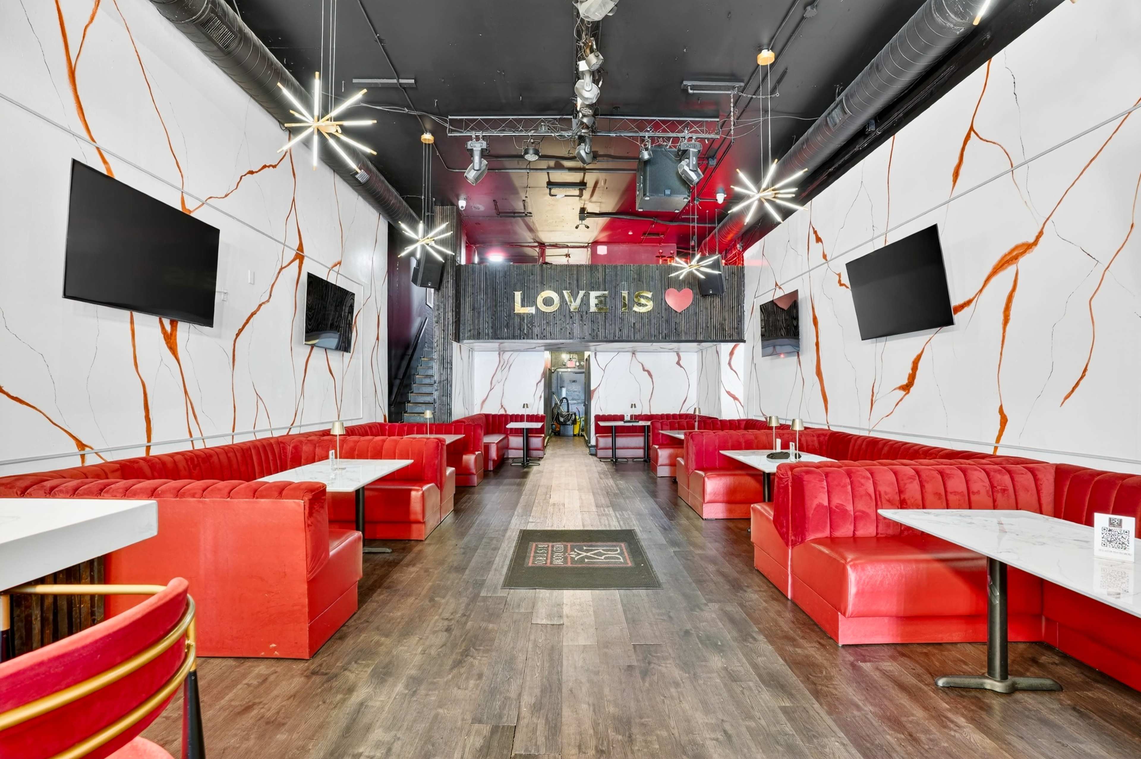 The image shows a restaurant interior with red booths, white tables, and decorative wall accents, including a "LOVE IS" sign and two televisions mounted on the walls.