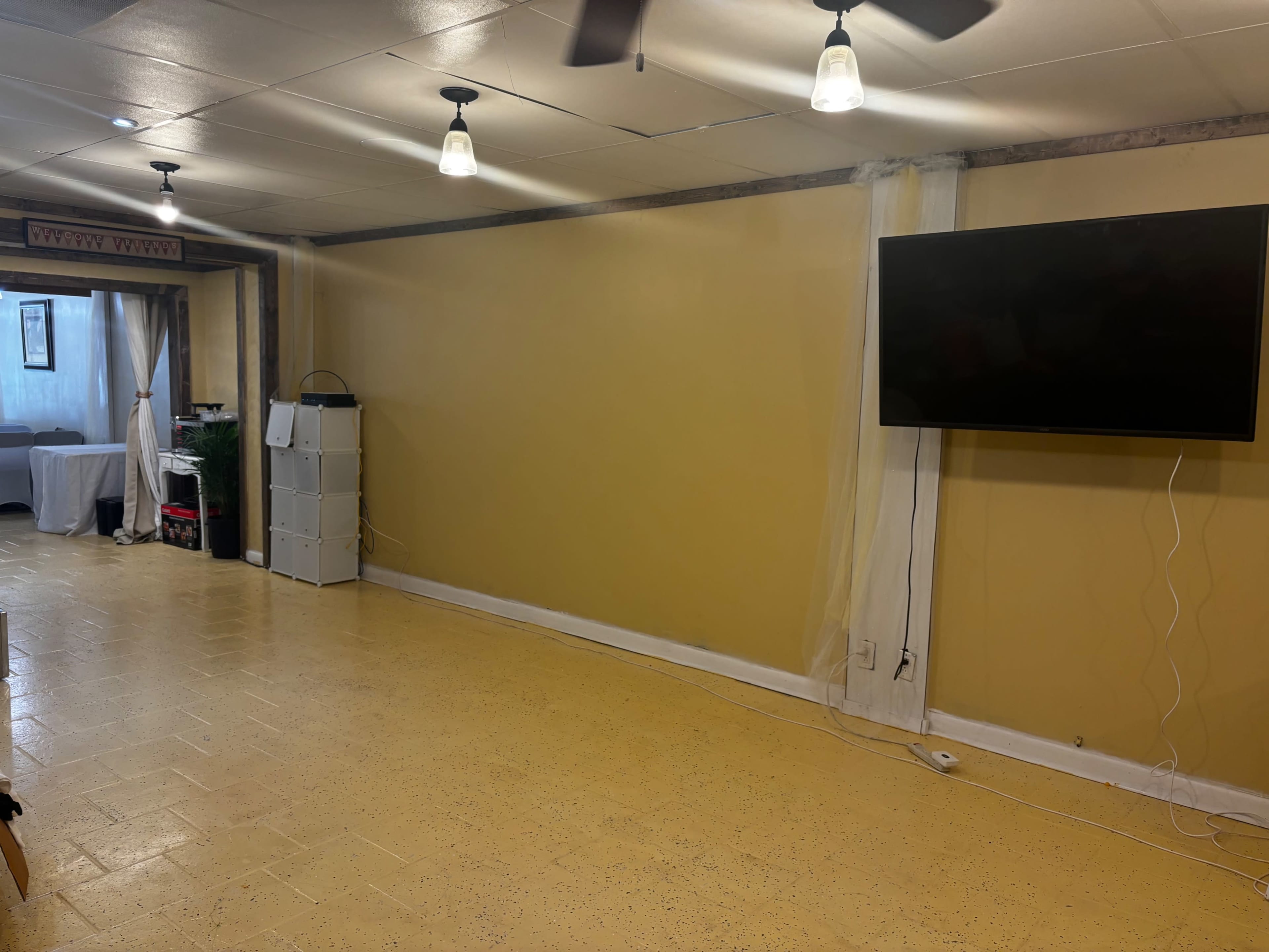 The image shows a sparsely decorated room with yellow walls, a large television mounted on the right side, and bare floor space.