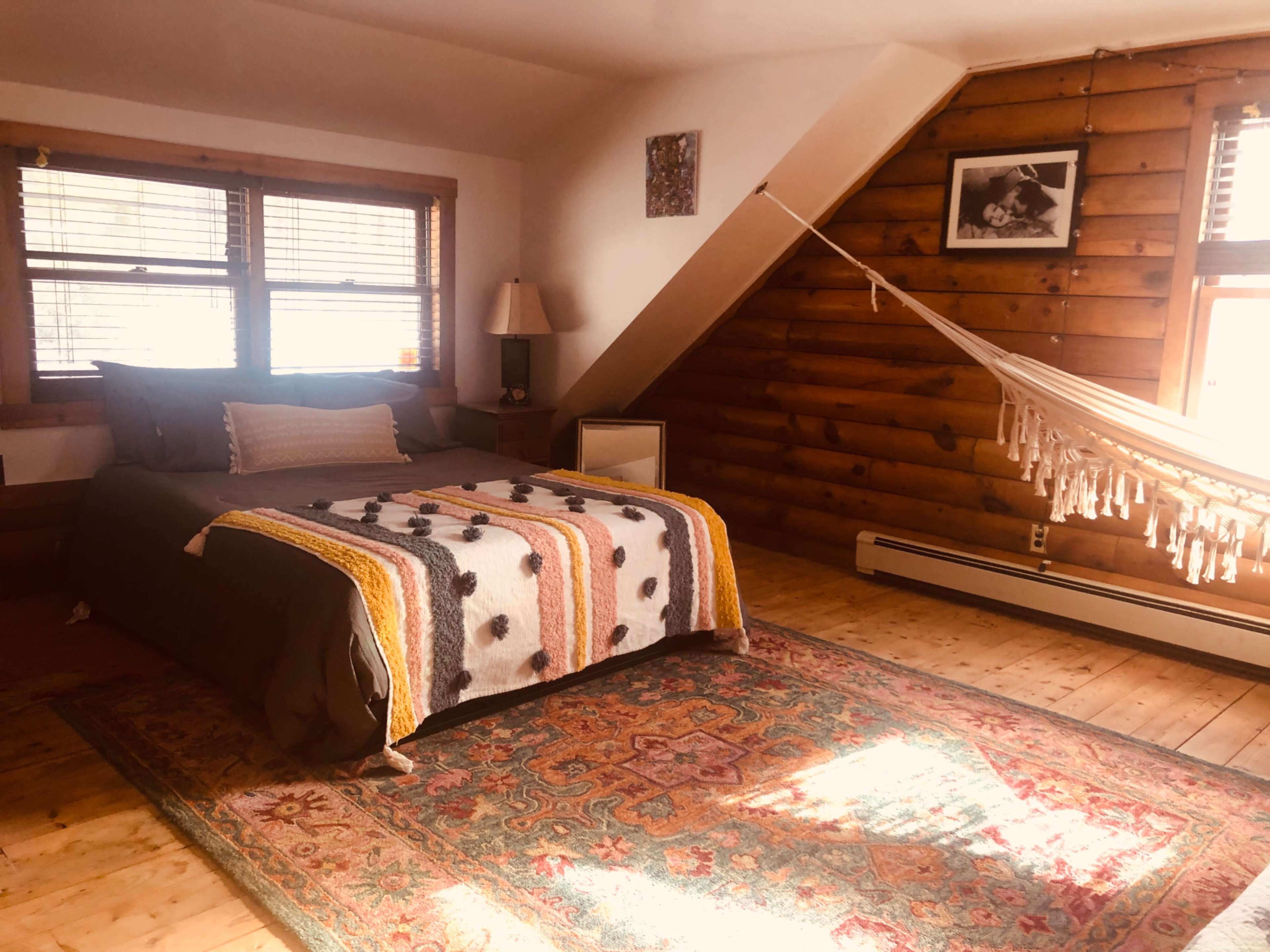 A cozy bedroom with a wooden accent wall, a bed adorned with a colorful blanket, and a hammock in the corner.