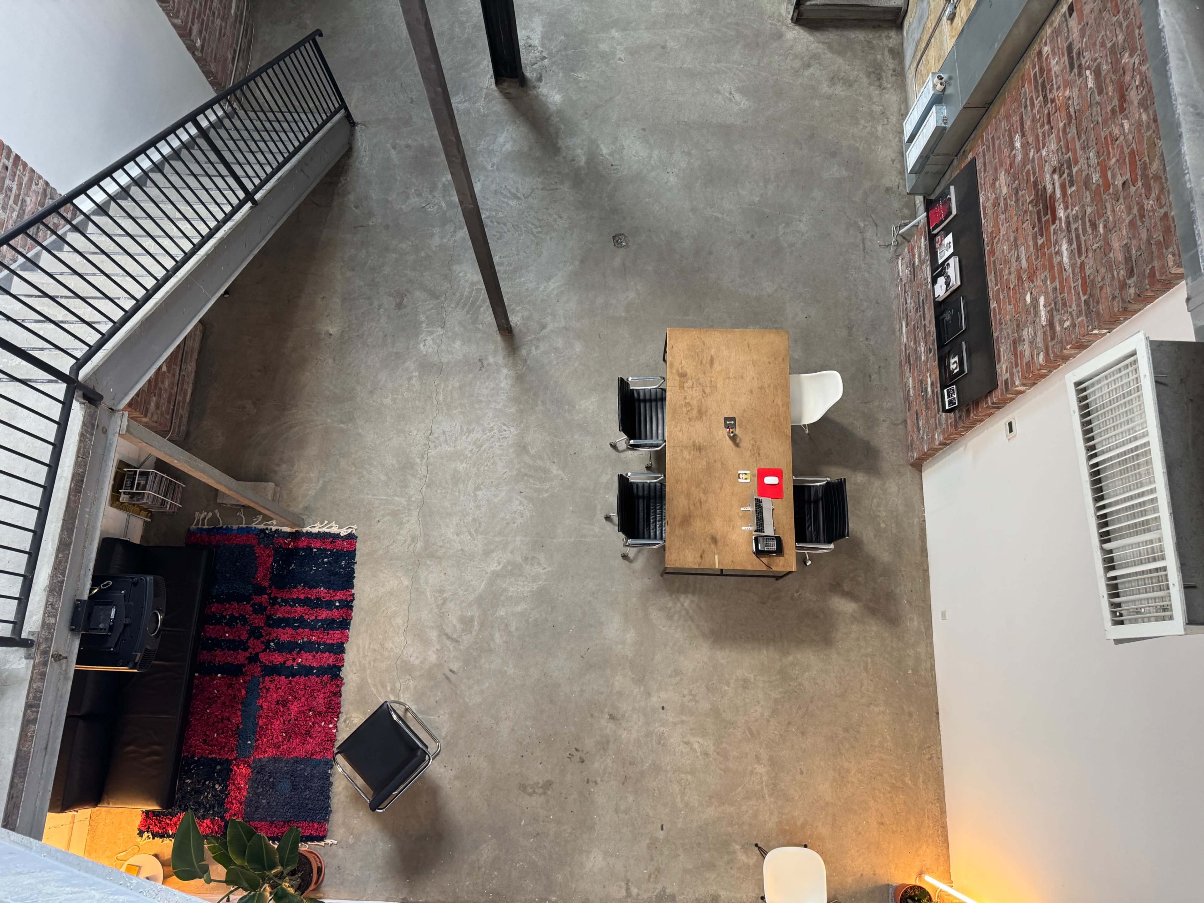 The image shows a spacious open area with a wooden table surrounded by chairs, polished concrete floors, and exposed brick walls.