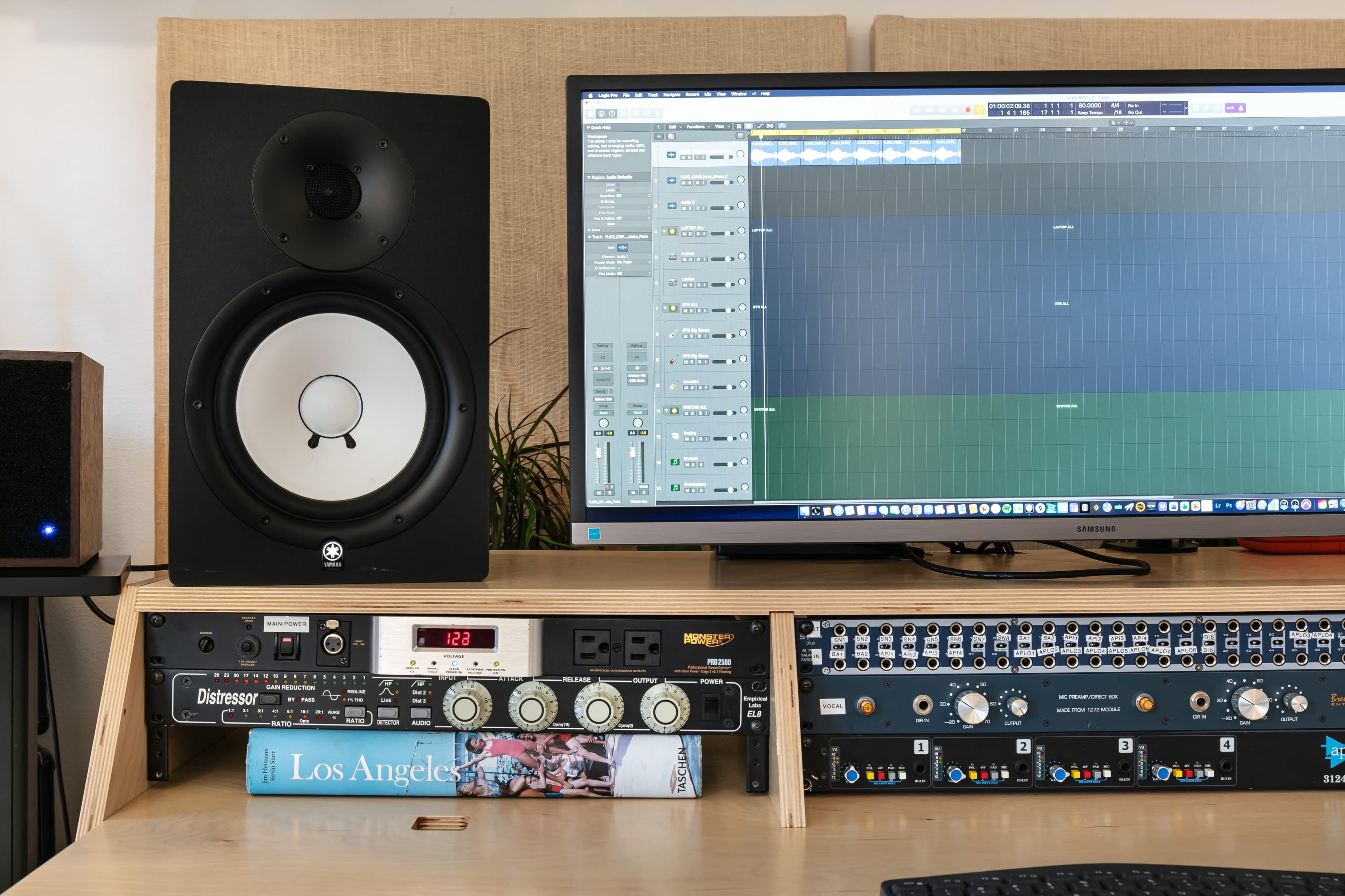 A music production setup with a monitor displaying audio editing software, a speaker, and a rack-mounted audio interface.