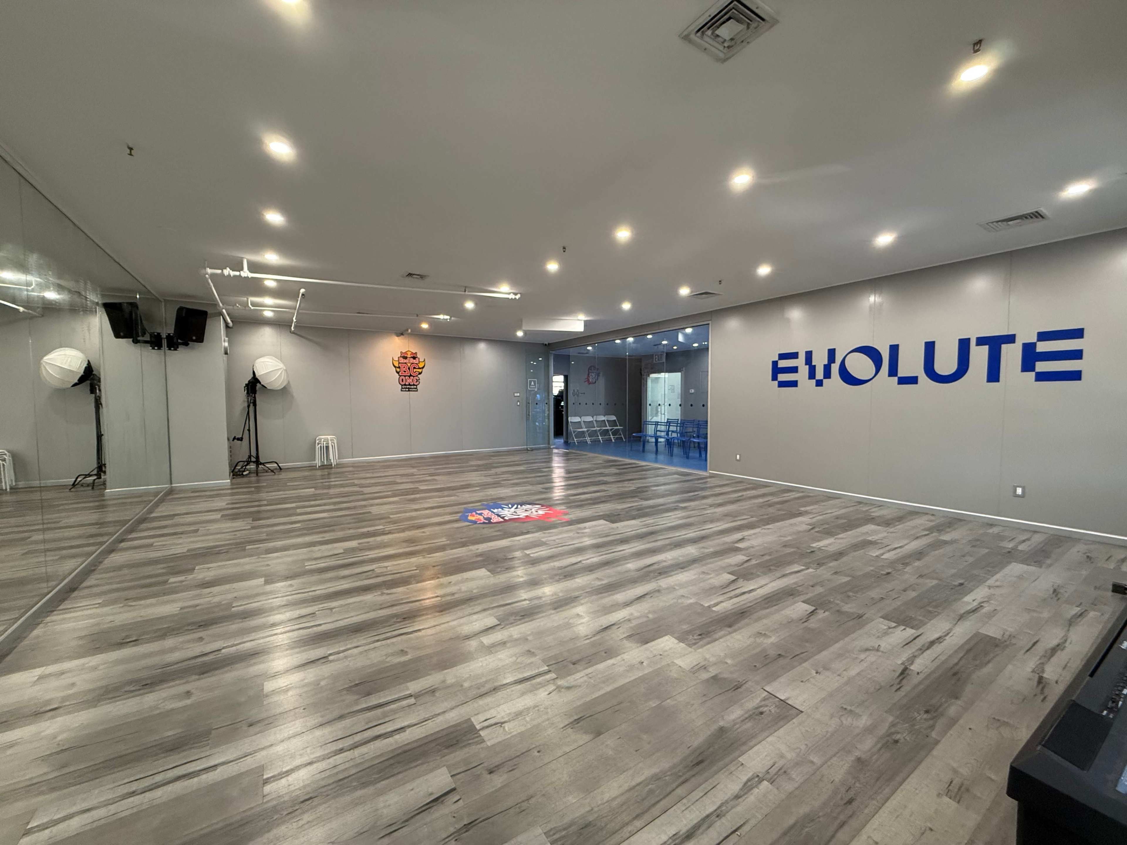 The image shows an empty studio space with wooden flooring, large mirrors on one side, and the word "EVOLUTE" prominently displayed on the wall.