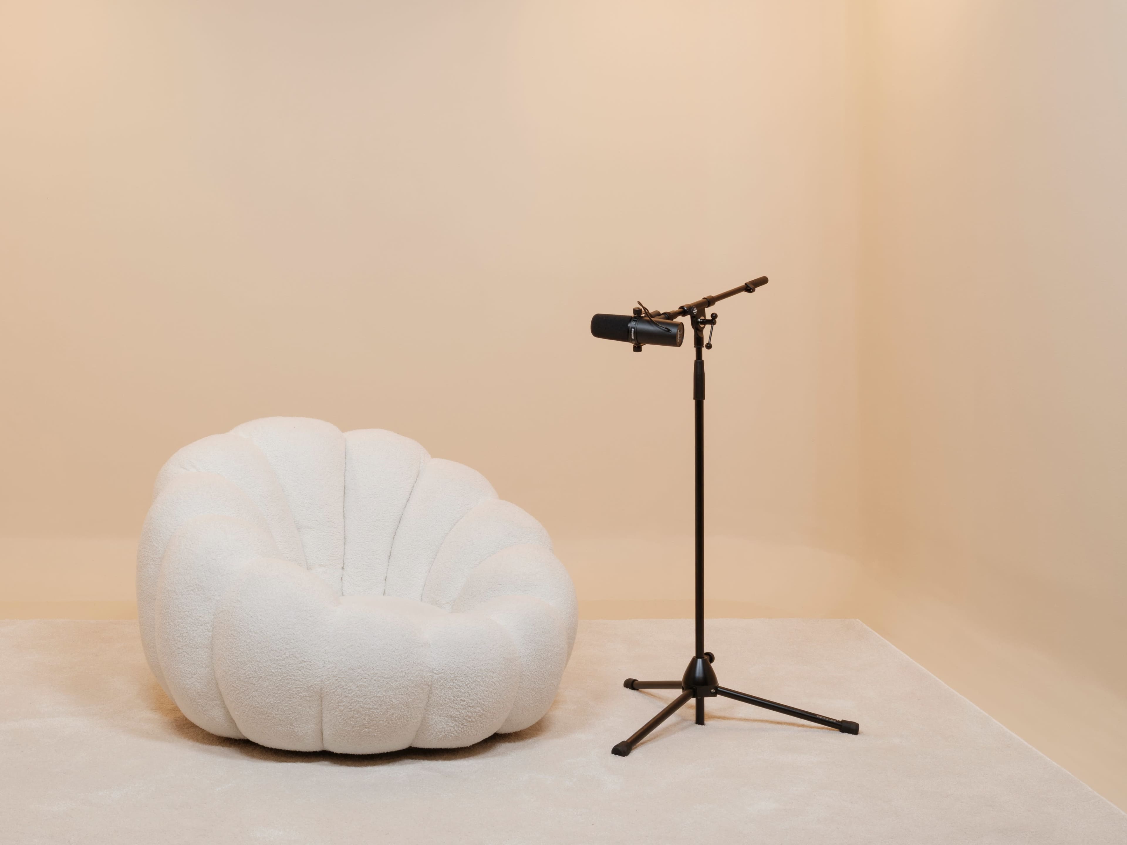 The image features a soft, white bean bag chair next to a black microphone mounted on a stand against a light-colored wall.