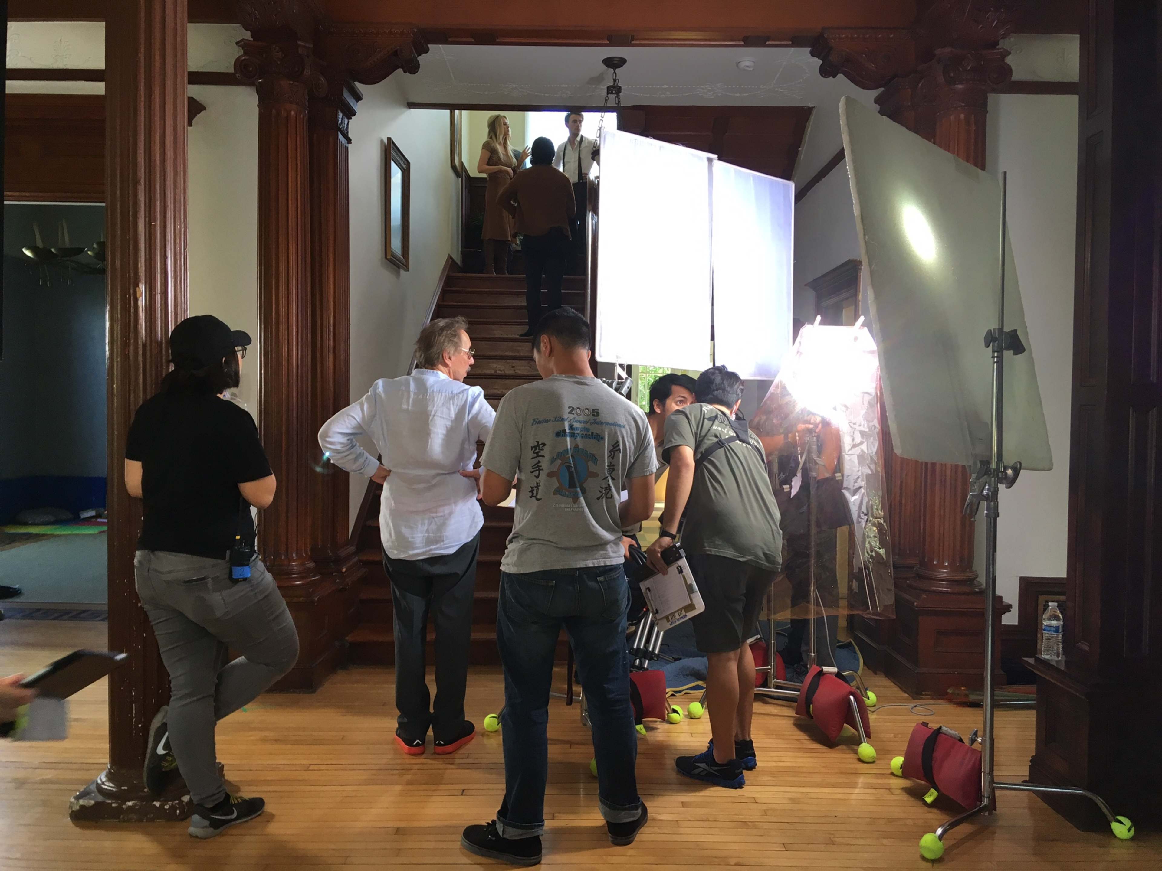 A film crew sets up equipment in a staircase area of a house while preparing for a shoot.
