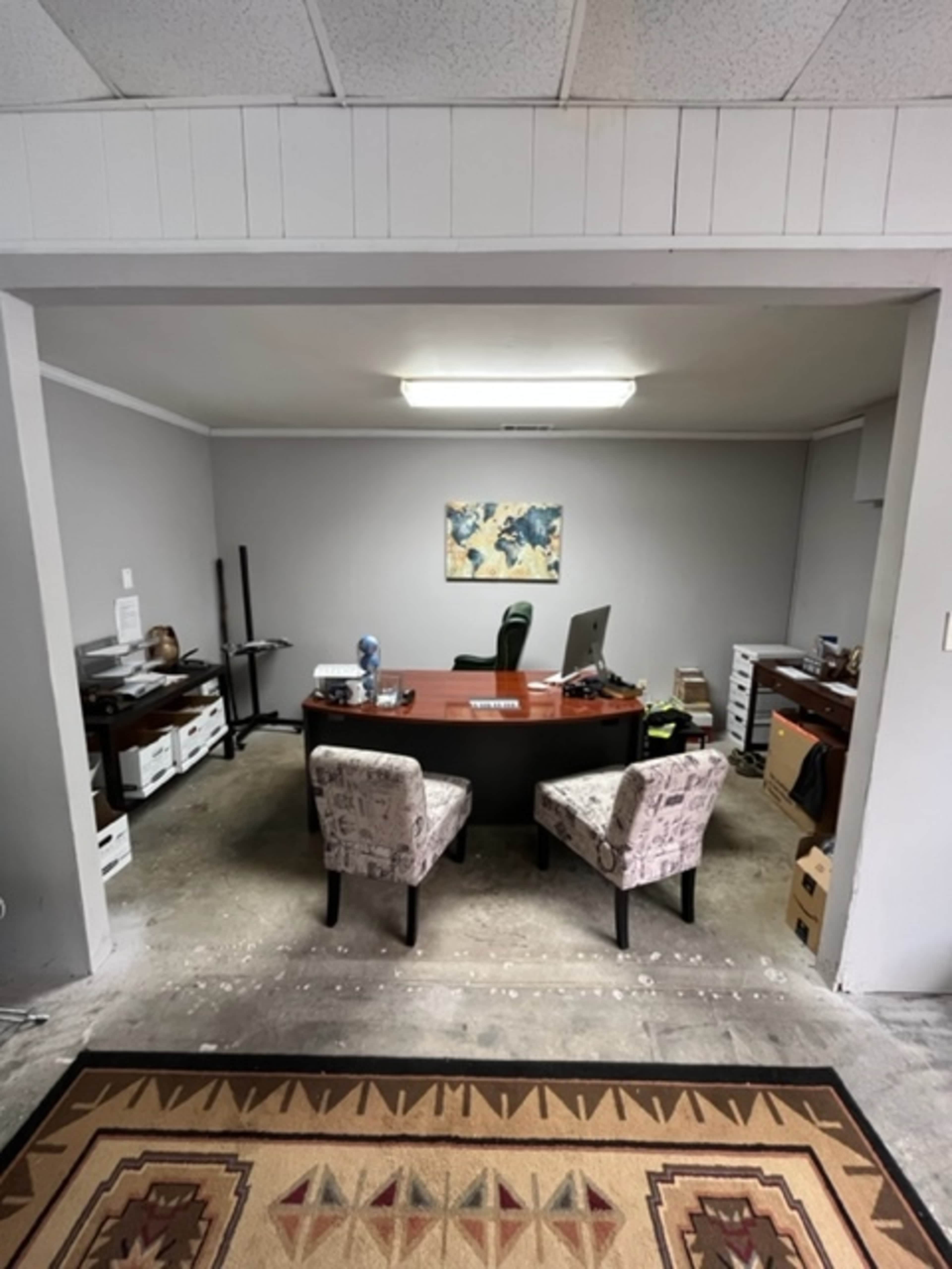 The image shows an office space with a desk, two patterned chairs, and storage boxes, all situated against gray walls.