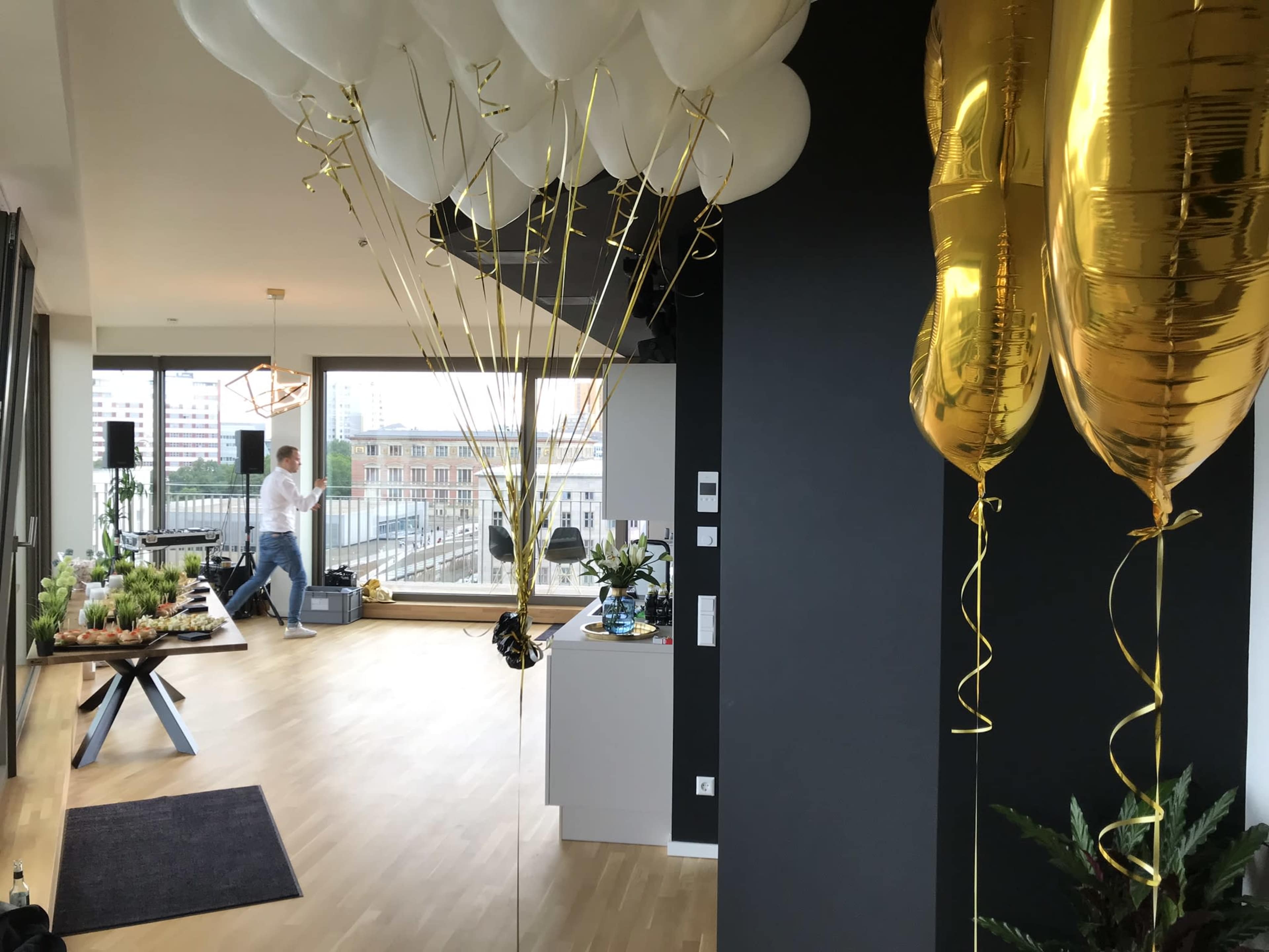 A modern event space with balloons tied to a table, a person in the background, and a view of a city through large windows.