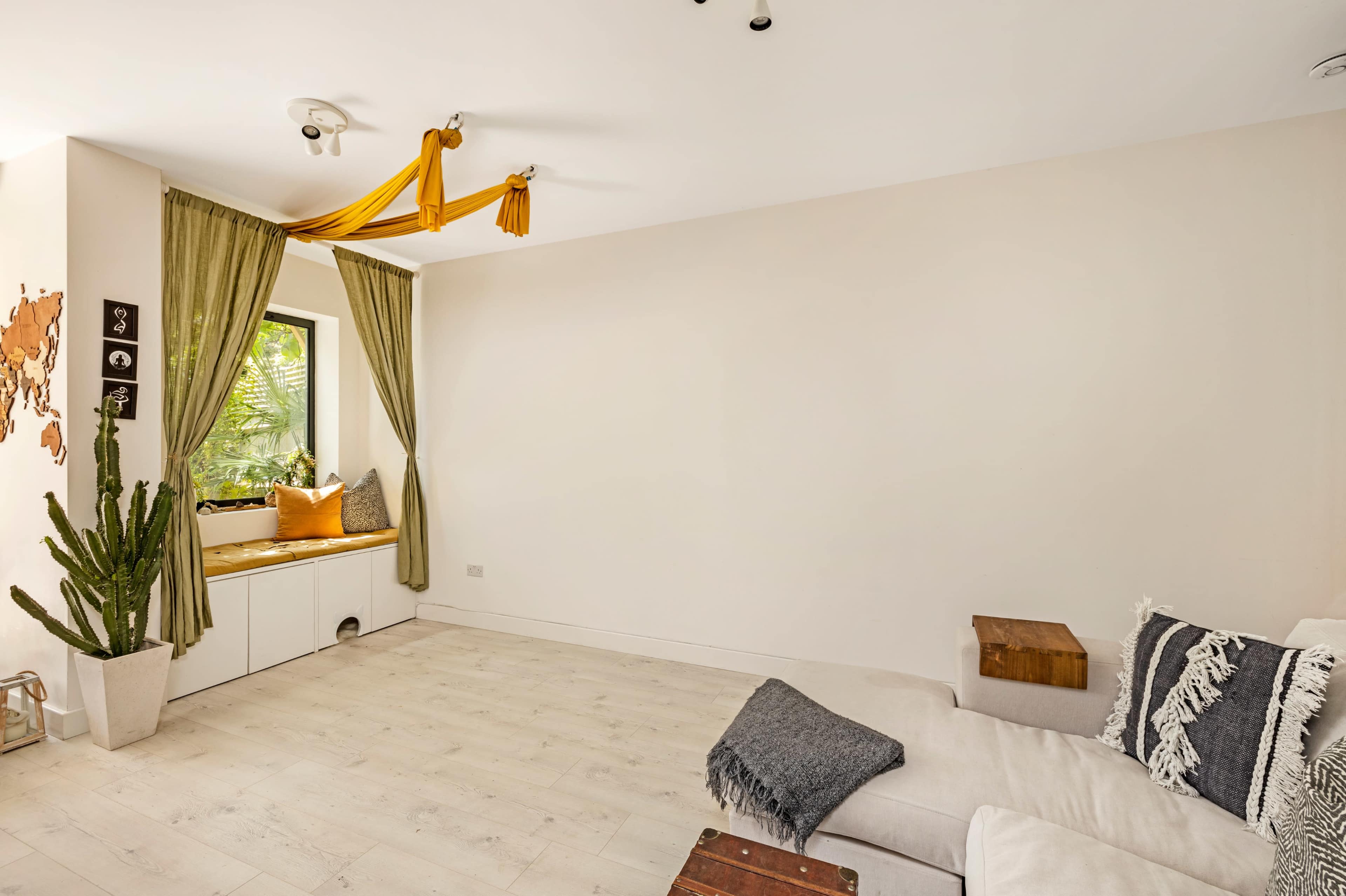 A bright room with a beige wall, a window seat adorned with cushions, a potted cactus, and a cozy white sofa.