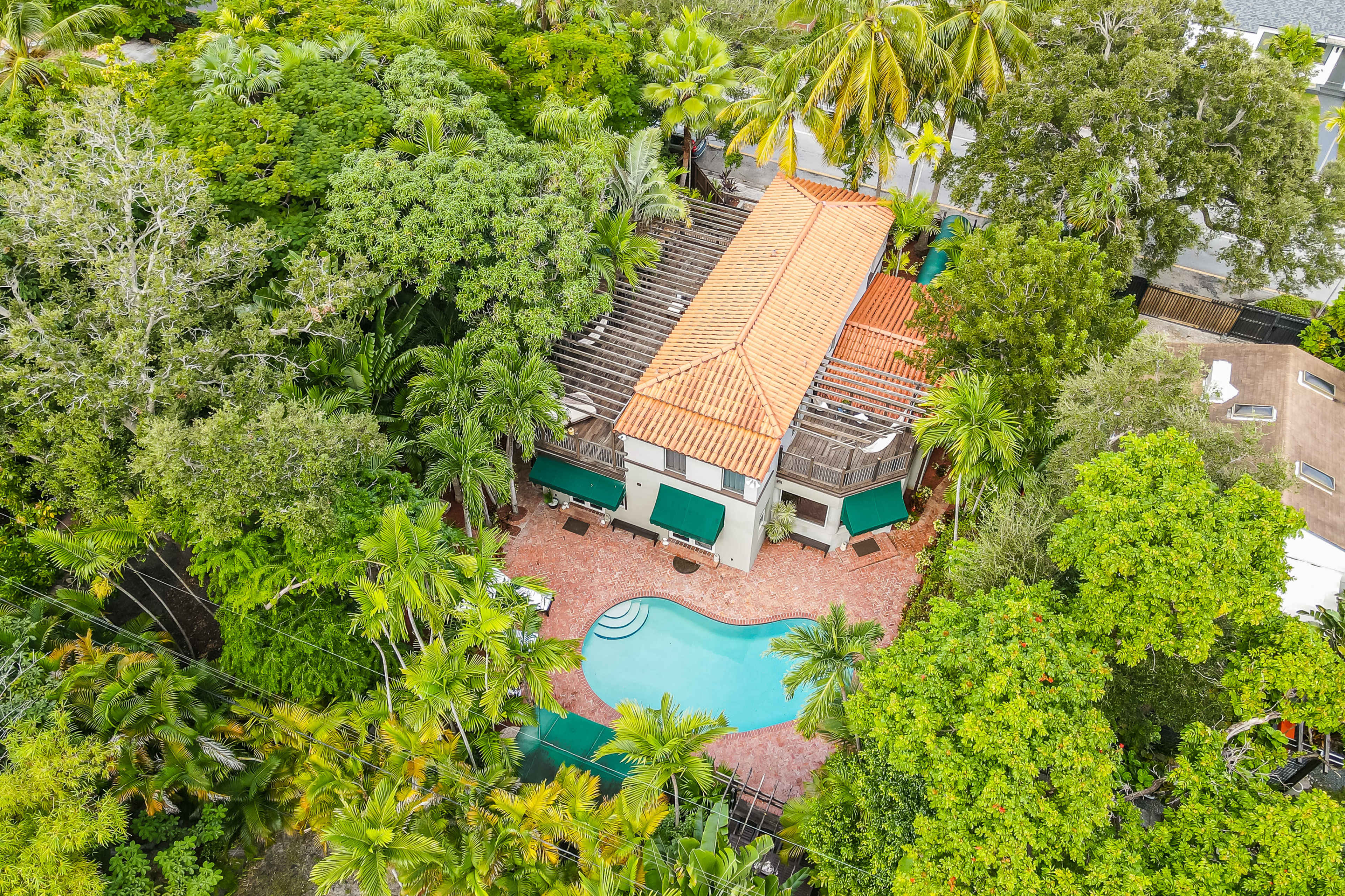 The image shows an aerial view of a house surrounded by lush greenery and featuring a swimming pool in the backyard.
