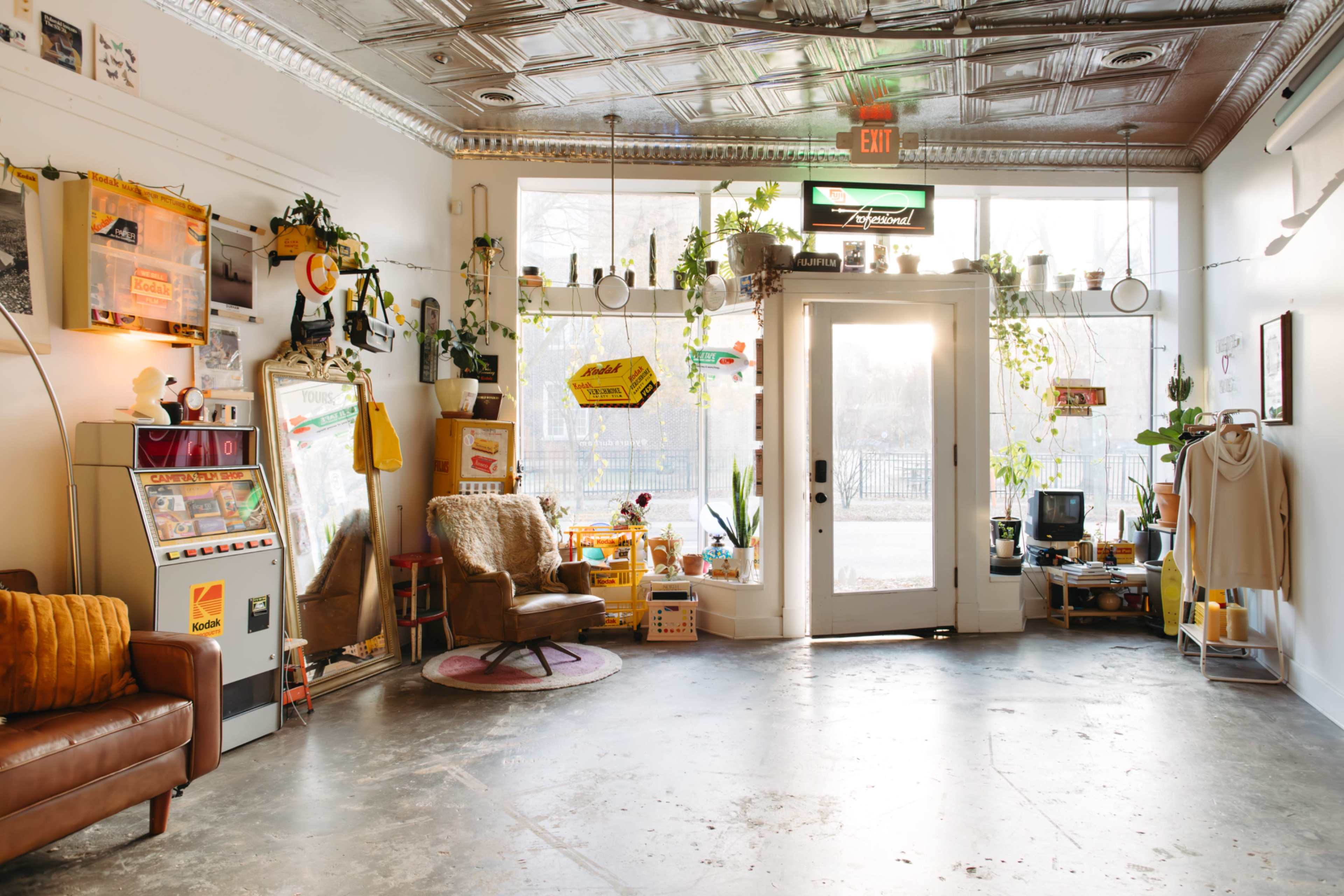 The image shows a cozy room filled with plants, vintage decor, and a welcoming entrance door.