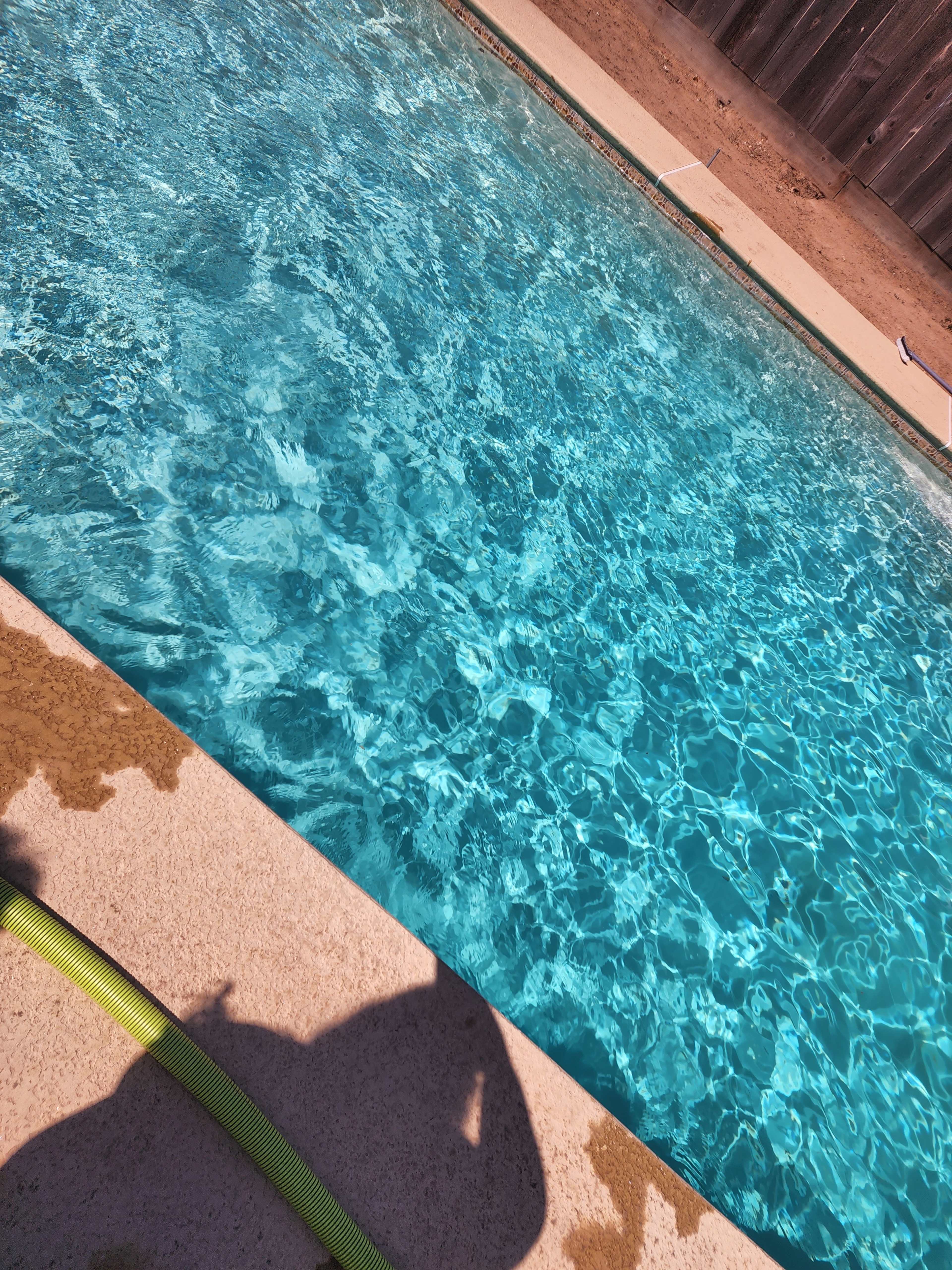 A clear swimming pool with sunlight reflecting off the water's surface and a shadow of a person beside it.